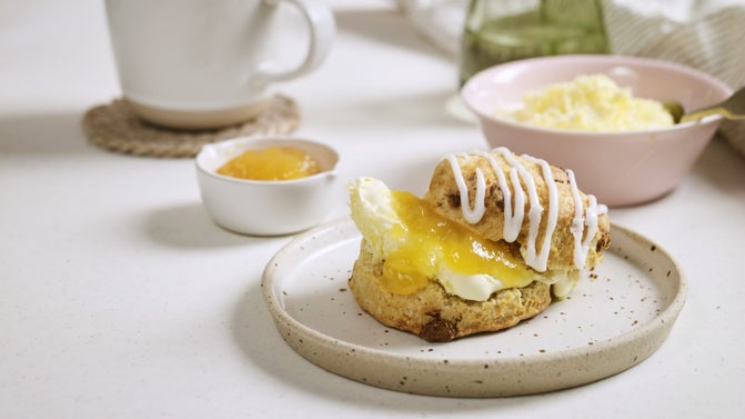 Lemon and white chocolate scones on a plate next to a serving dish and tea cup
