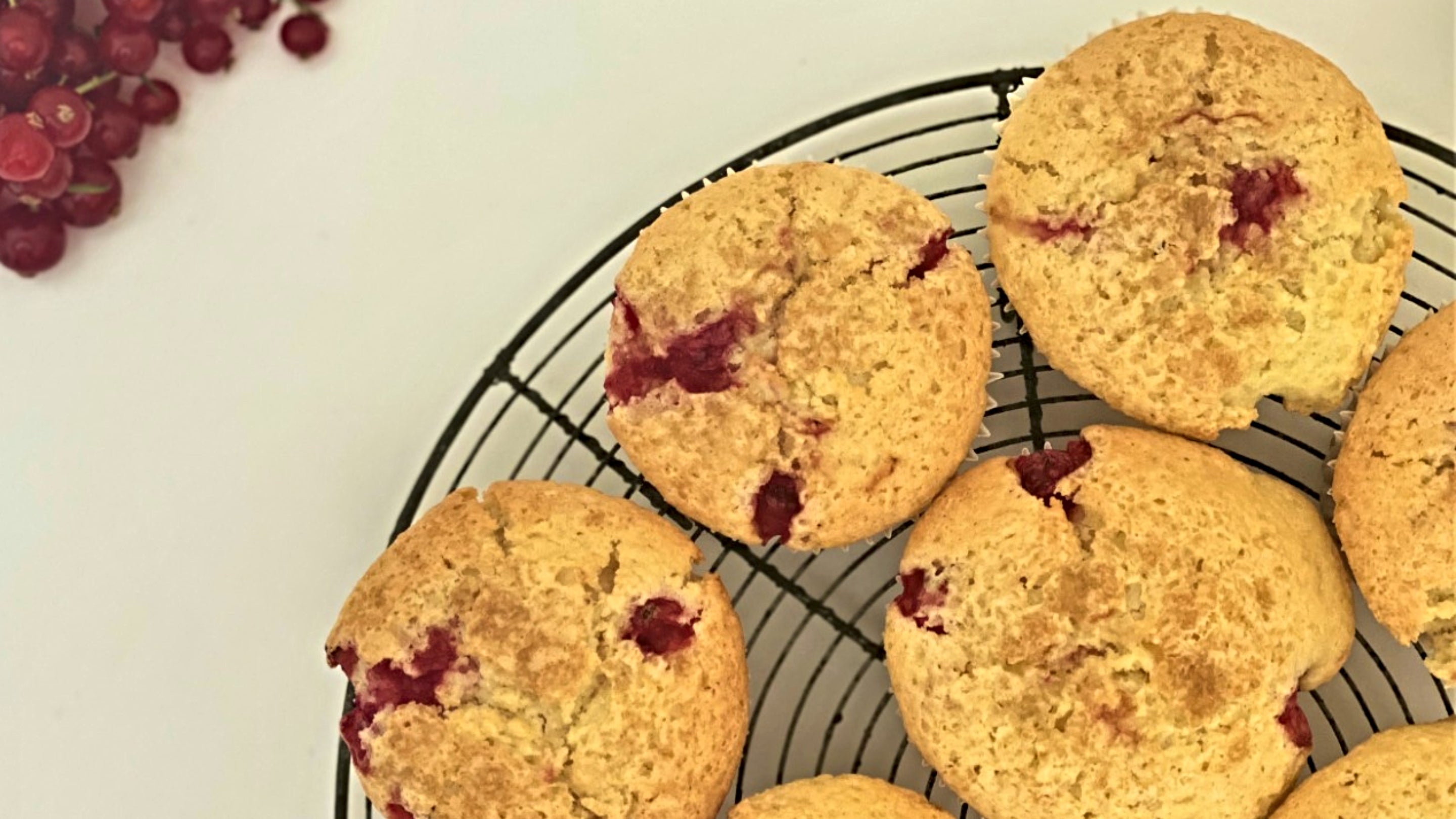 Redcurrant muffins on a rack, viewed from above, with redcurrant pieces, and a bunch of redcurrants to the left