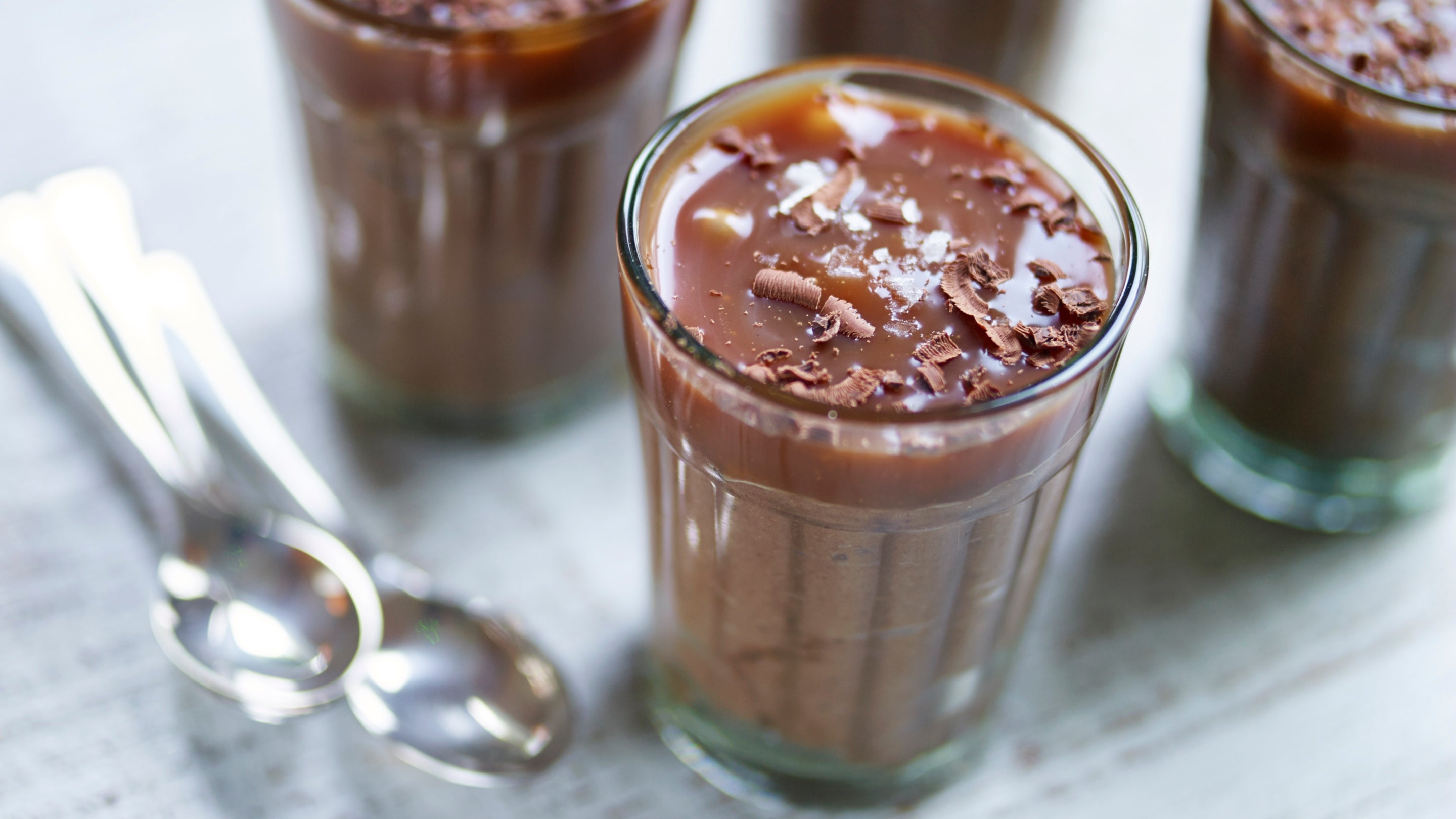 Four glasses filled with mousse, topped with a layer of salted caramel, sprinkled with chocolate chips and salt