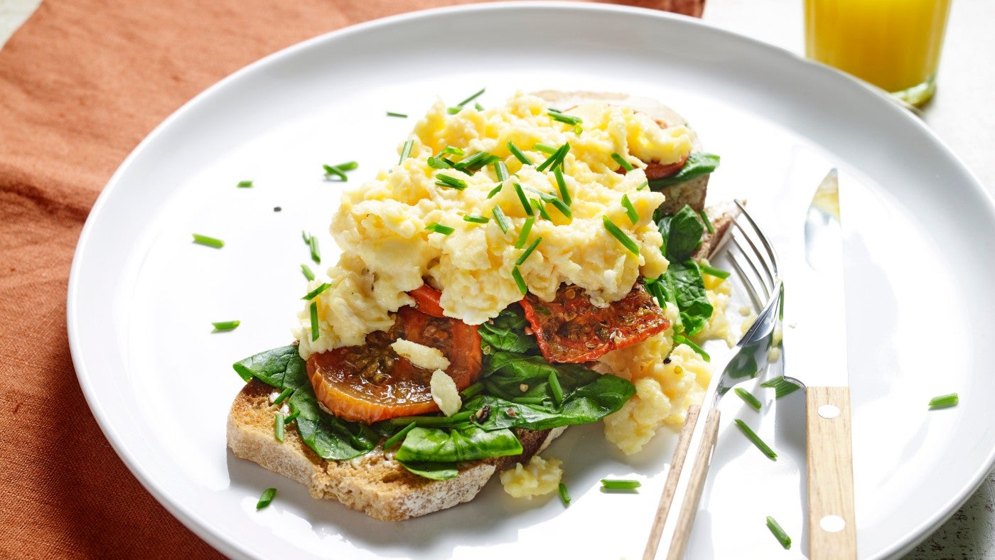 Scrambled egg with tomato and spinach on sourdough toast, on a plate with a knife and fork