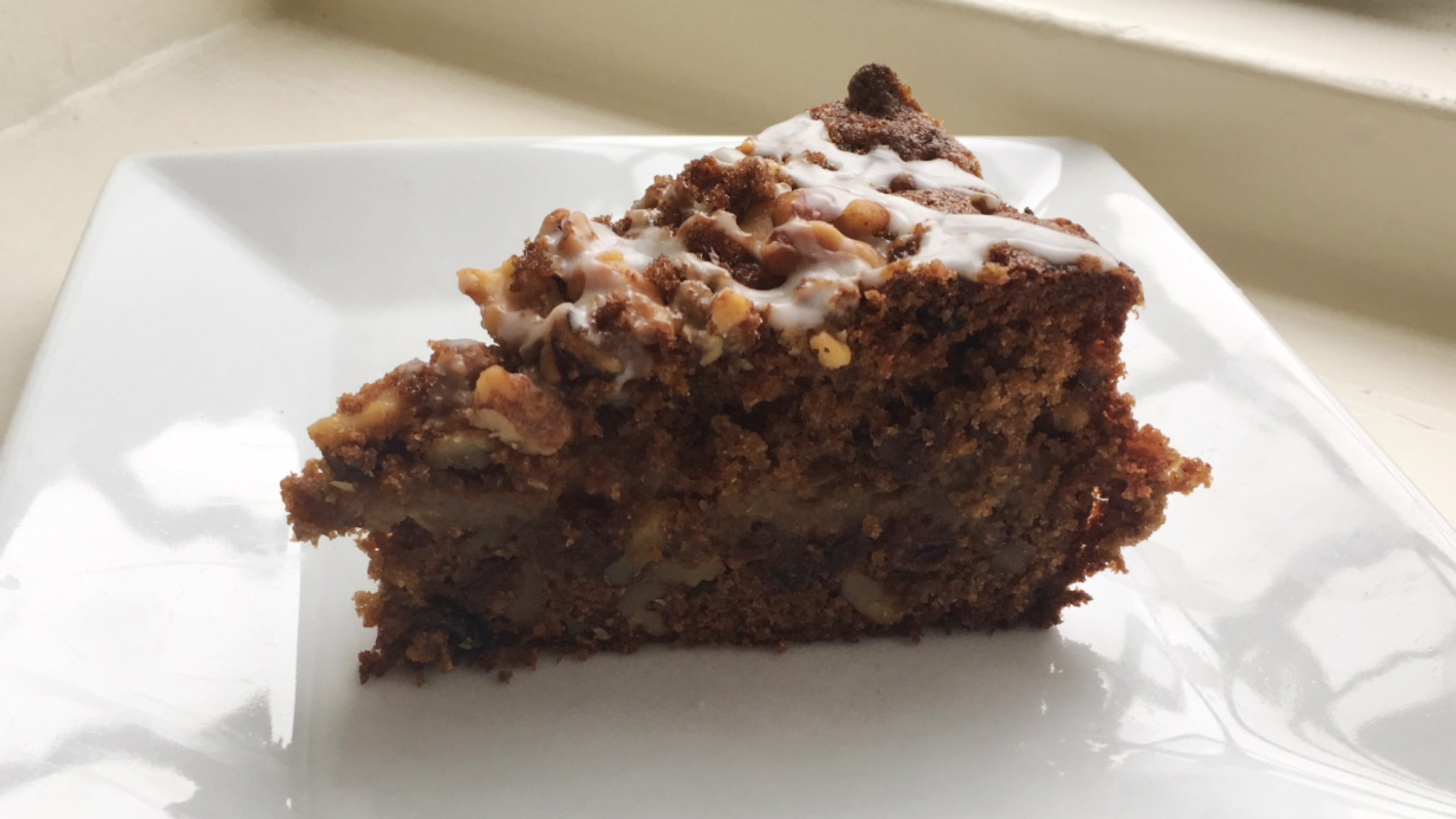 A slice of Standen Sussex apple cake, with walnut and apple pieces in it, on a white plate
