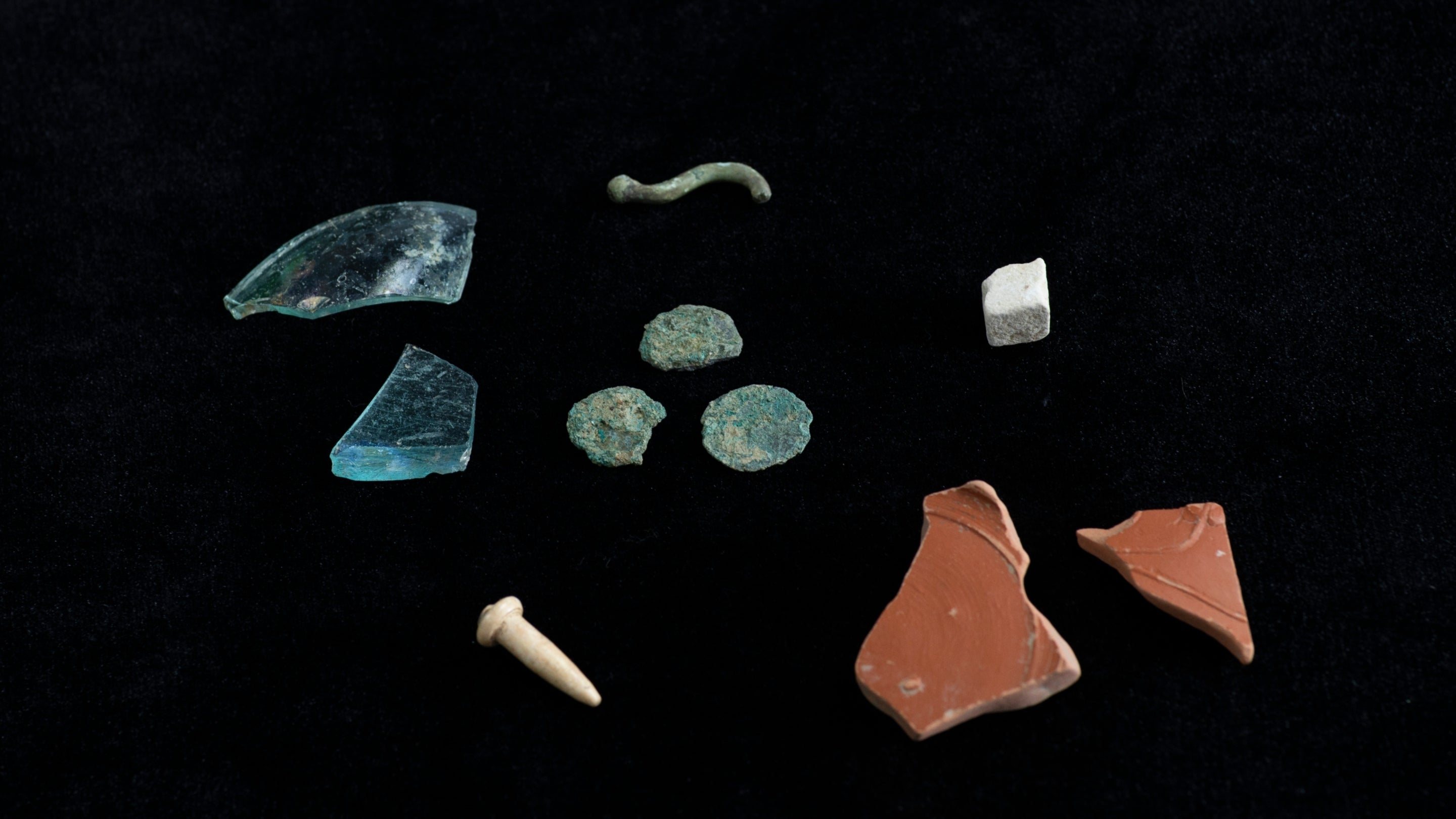 Fragments of ceramic, stone and glass Roman artefacts against a black background.