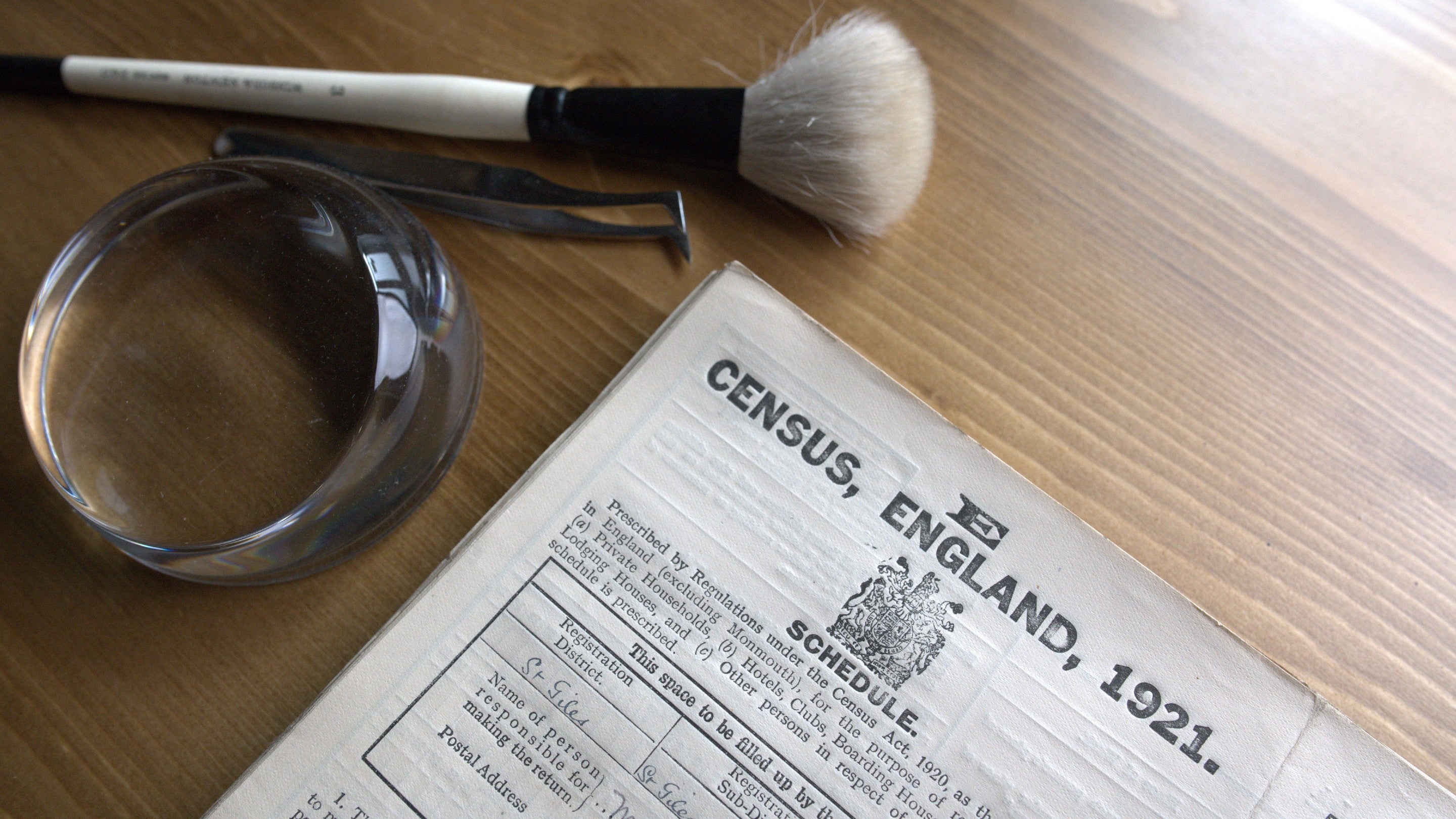 1921 Census records for England on a wooden table with a magnifying glass and brush laid above it