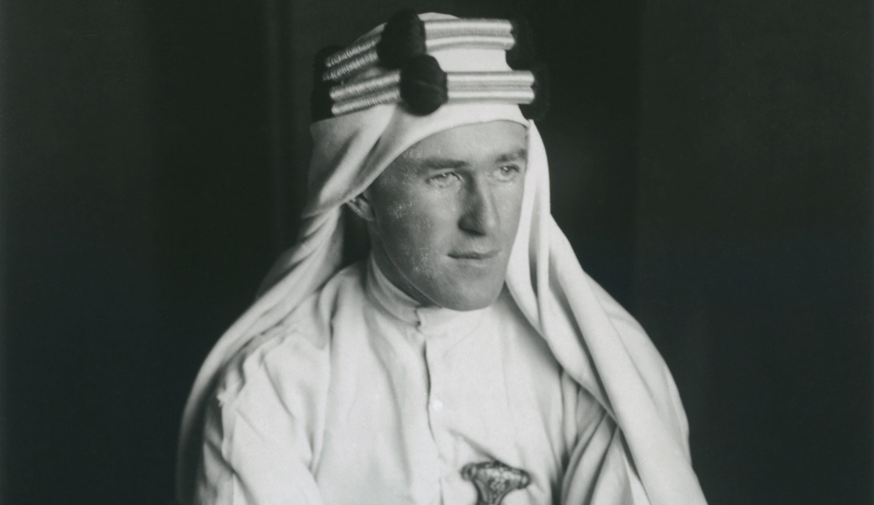 Black and white portrait photograph of T. E. Lawrence dressed in Arabian style clothing.