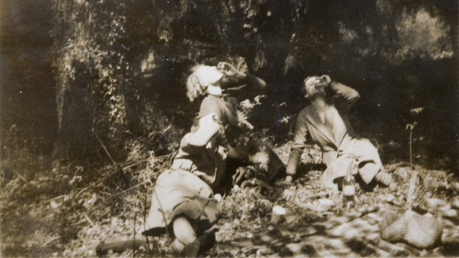 Black and white photograph of three women sitting in the countryside drinking from glasses