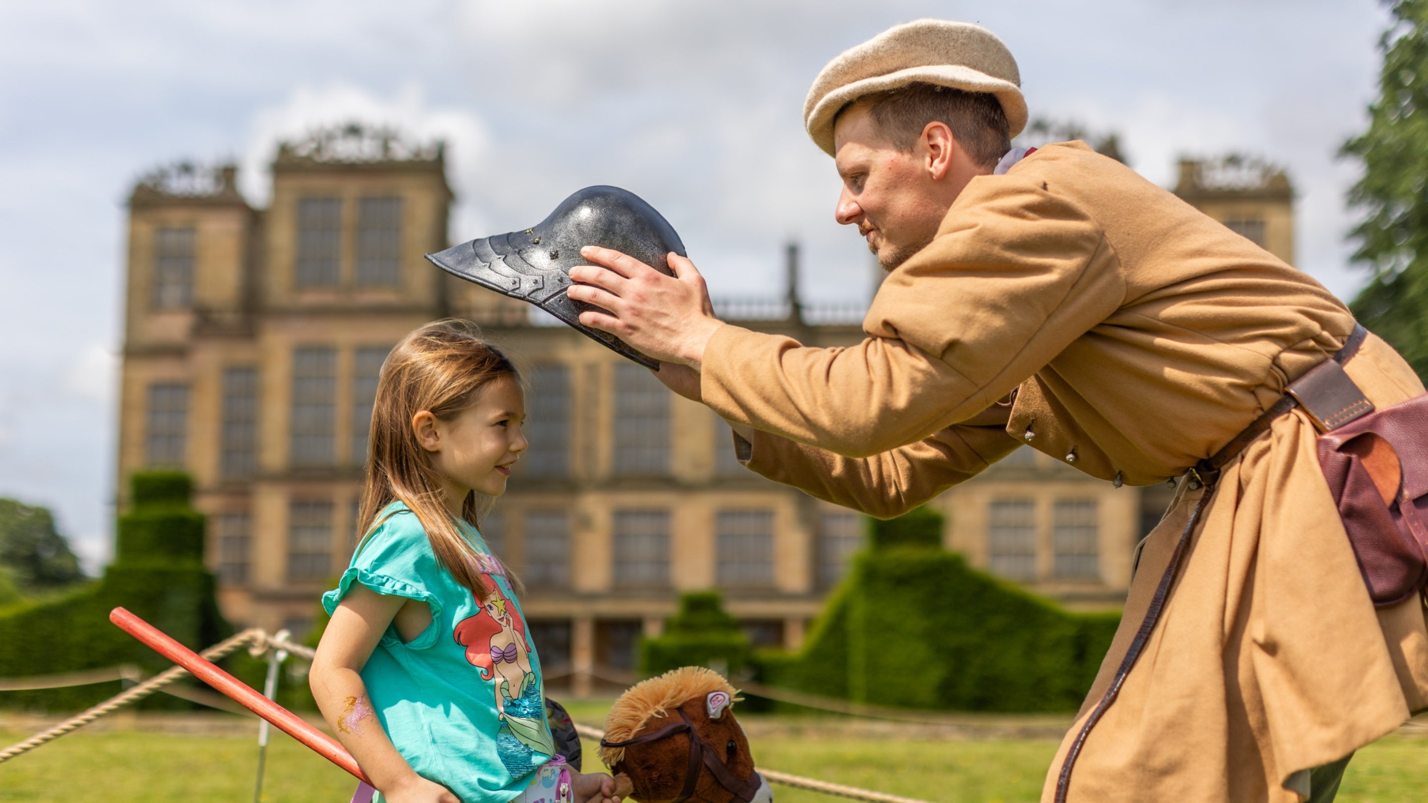 A historical reenactor placing a helmet on a smiling girl during the Festival of Archaeology at Hardwick Hall, Derbyshire