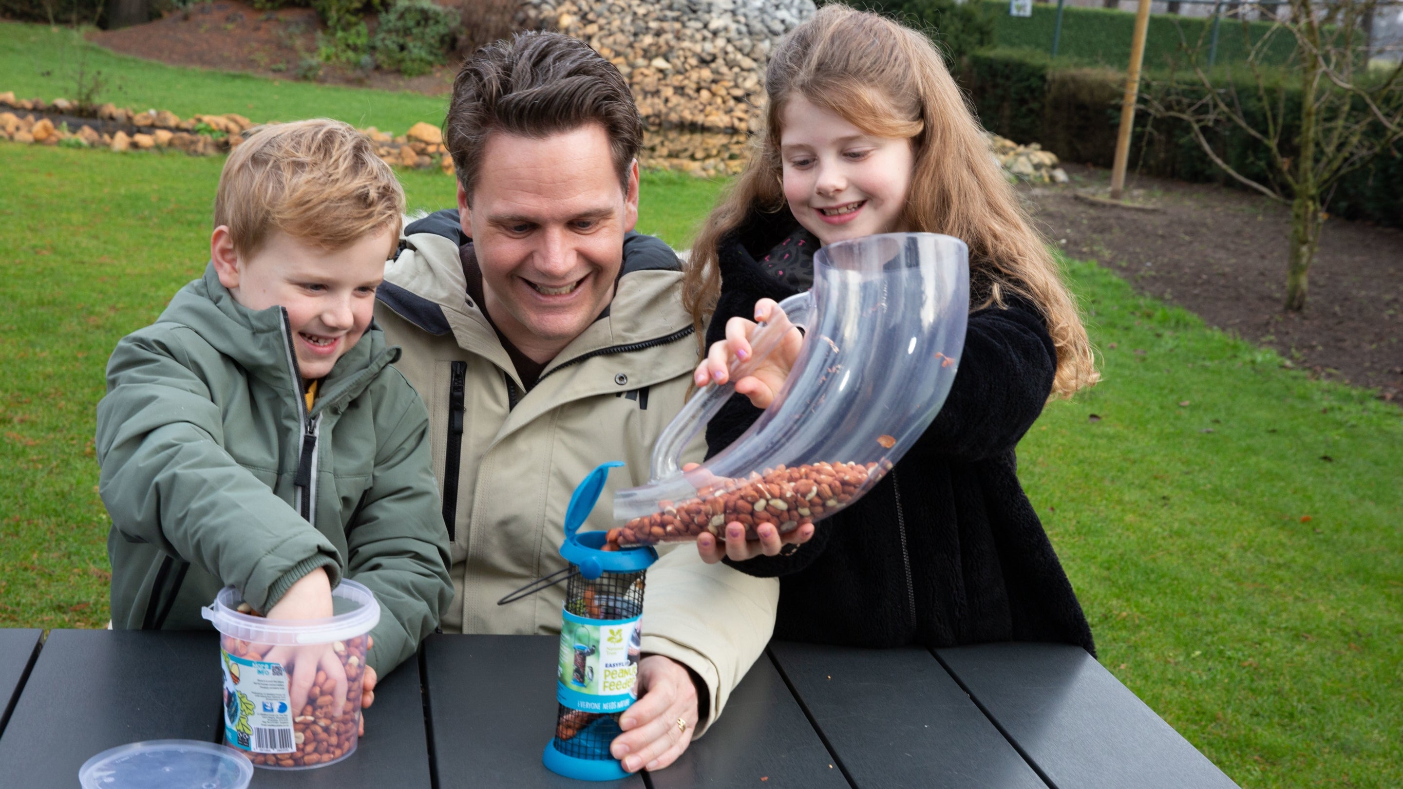 A father and two children fill up a blue bird feeder