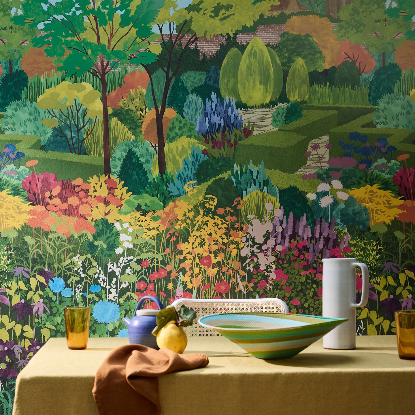 A table set for breakfast sits in front of a heavily patterned wallpaper showing a multicoloured castle garden