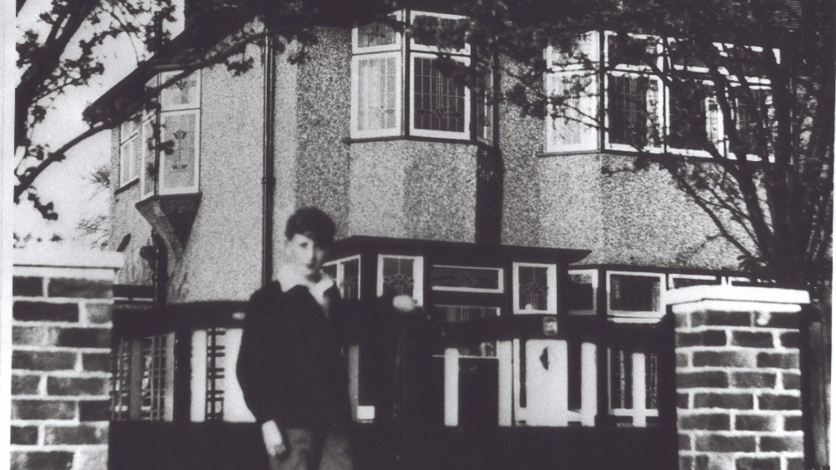 John Lennon as a child stands in front of the gates outside of Mendips