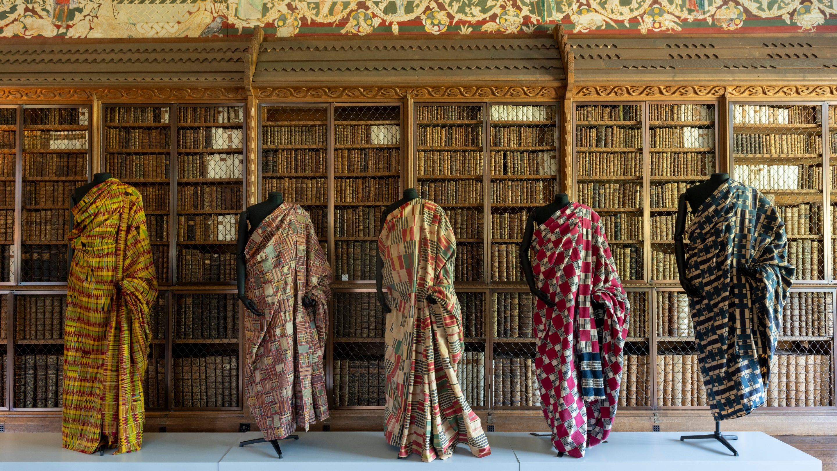 Five mannequins line up against a bookcase at Blickling, wearing colourful African textiles