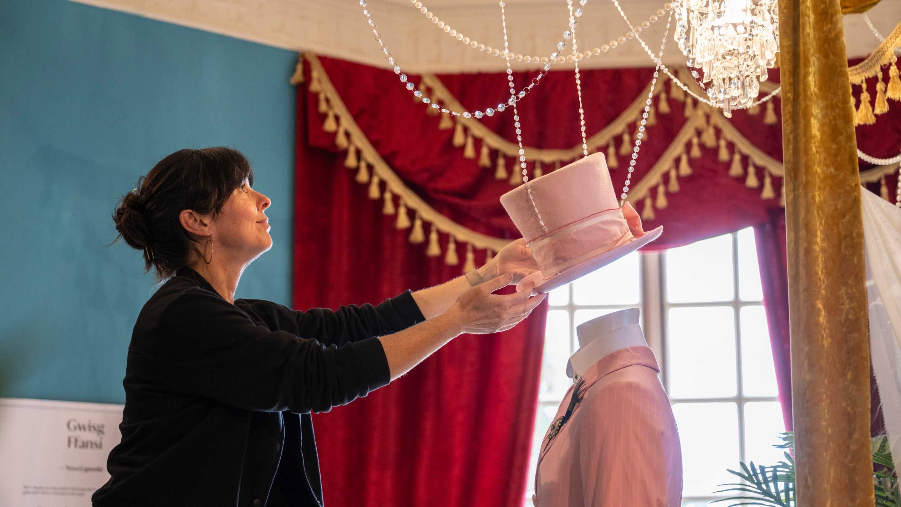 Exhibition designer places a pink top hat onto a mannequin, finishing off the costume display.