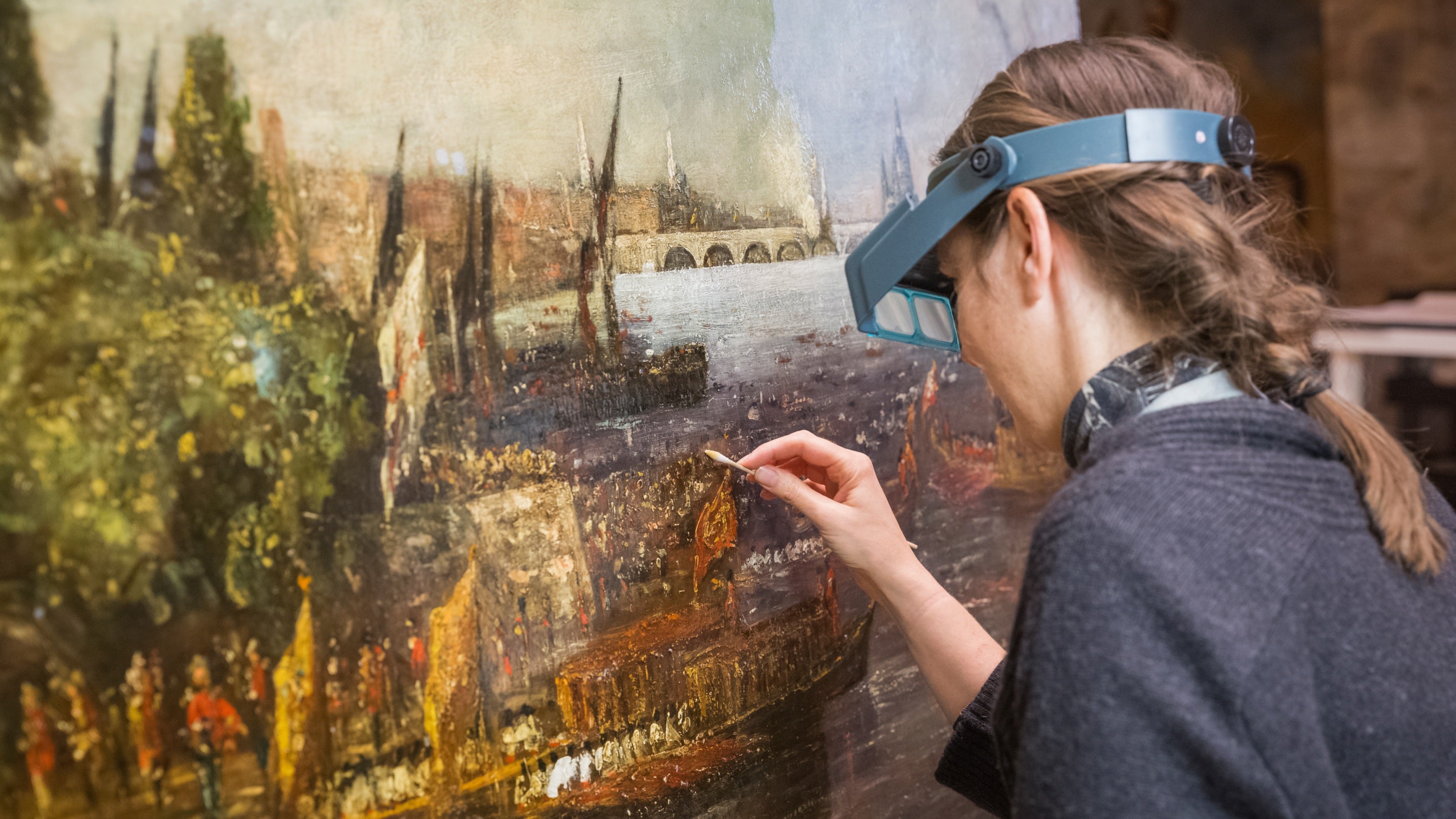 An expert wearing special goggles cleaning an oil painting