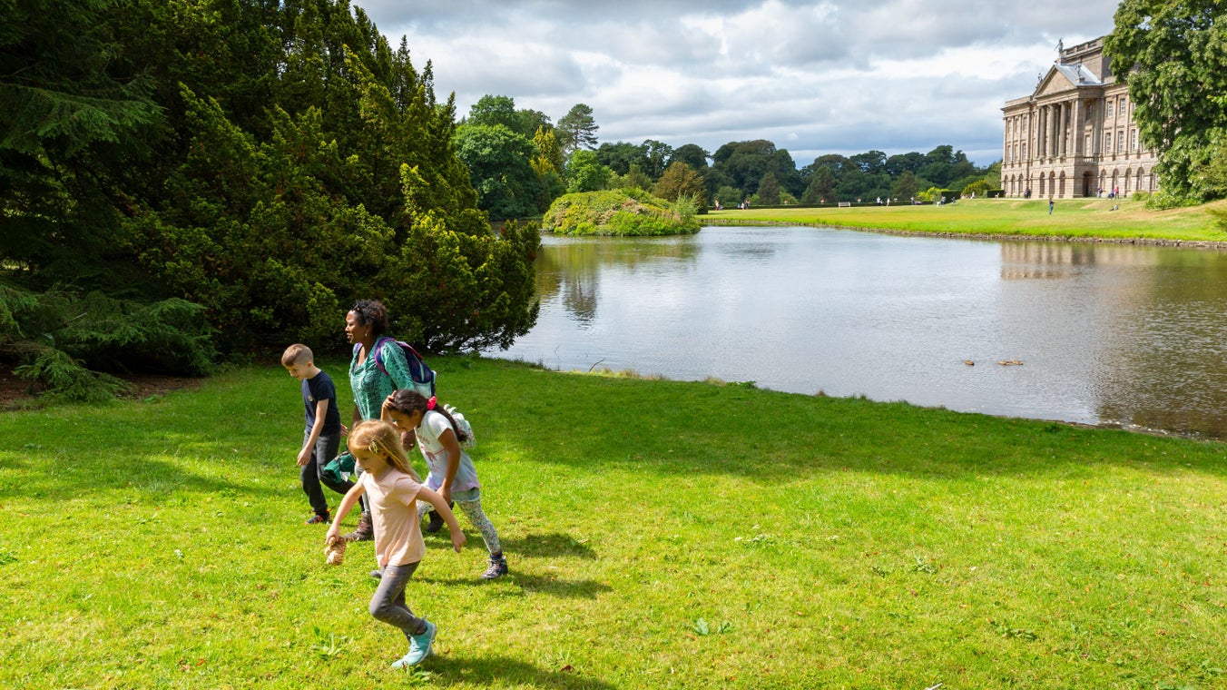 Kids running on the open green land near the lake in front of Lyme Park Mansion