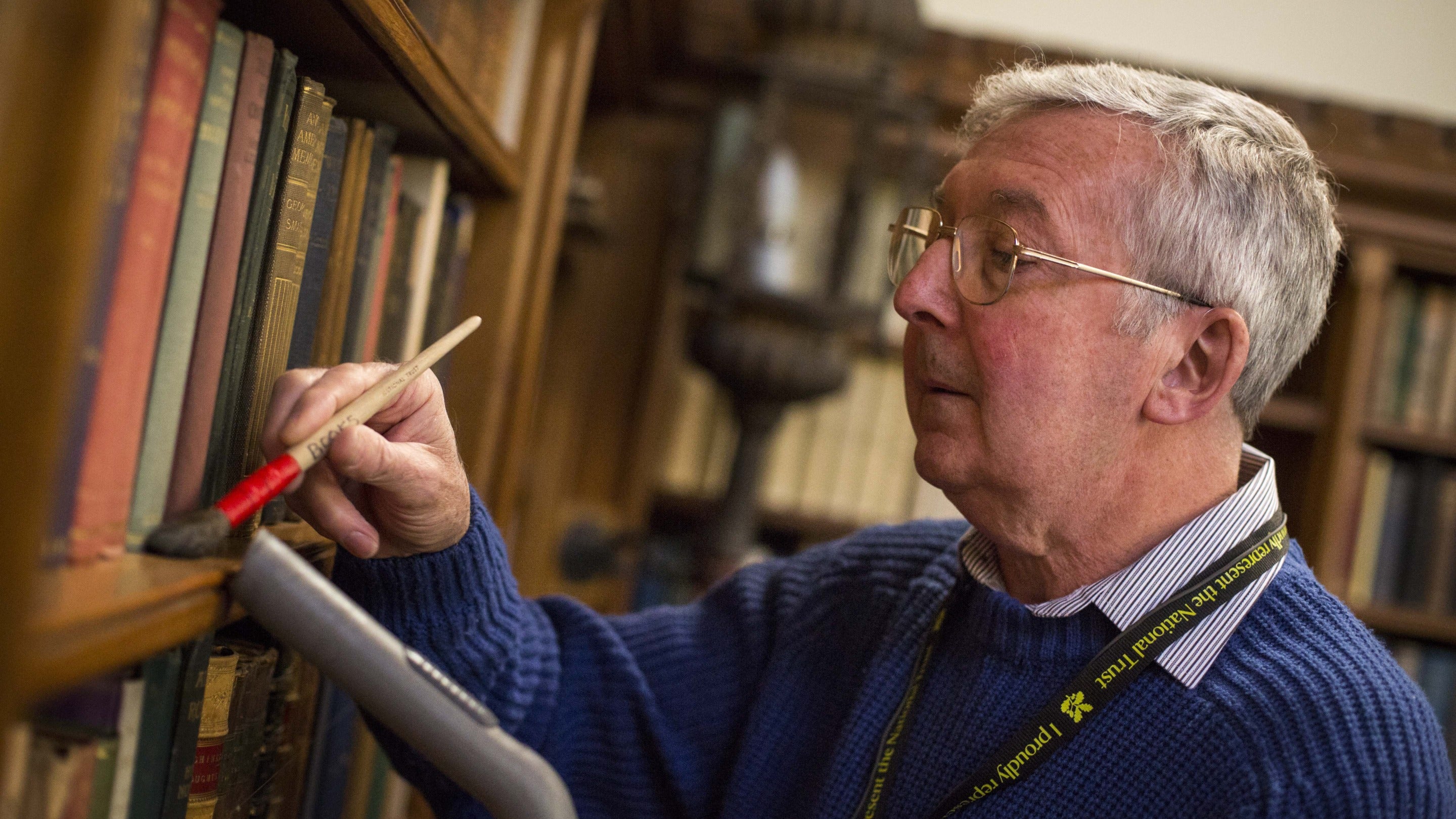 A volunteer carefully cleans books using a small brush and vacuum cleaner at Tyntesfield, Somerset