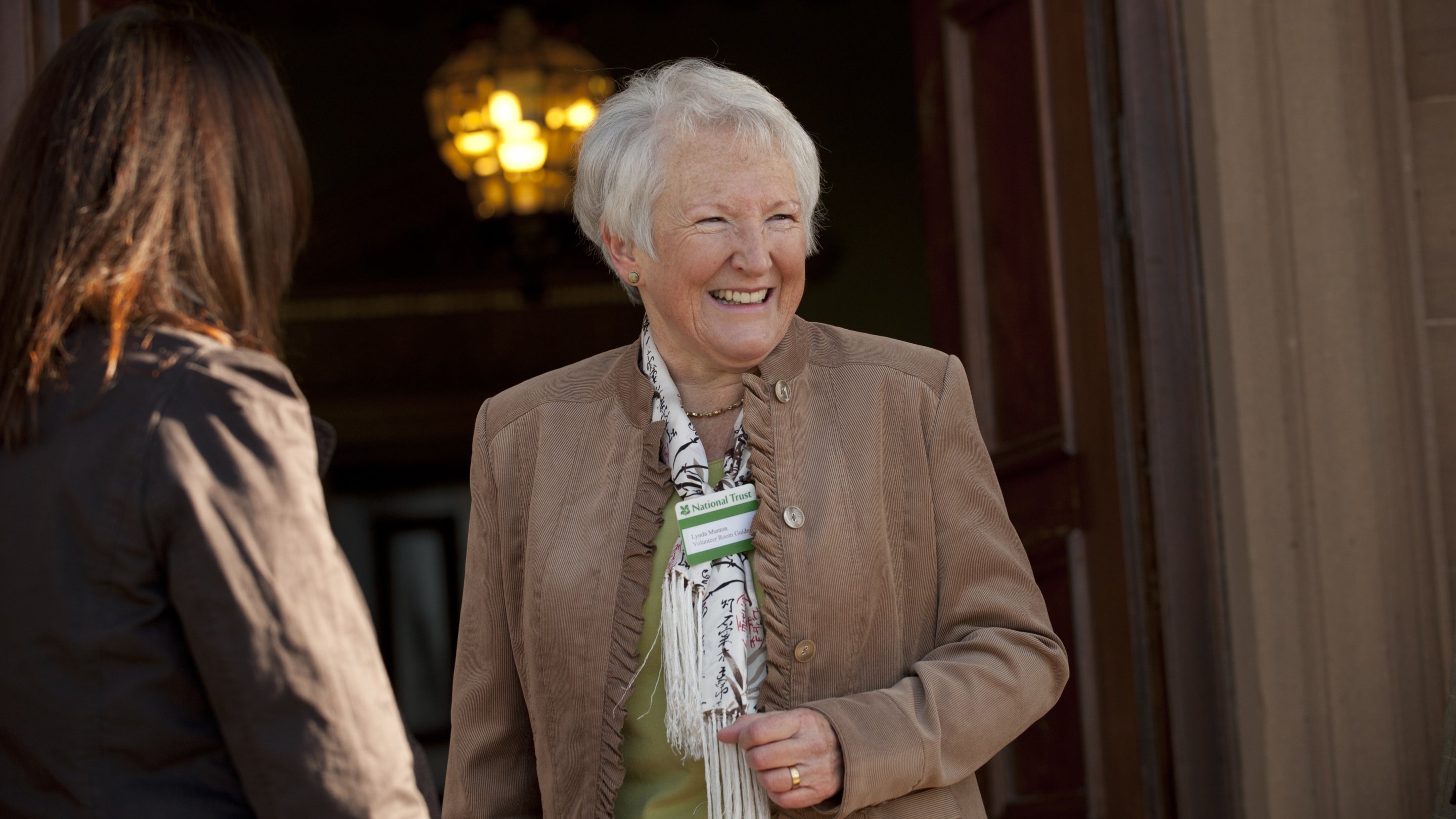 A female volunteer room guide standing in a doorway talking to a visitor.