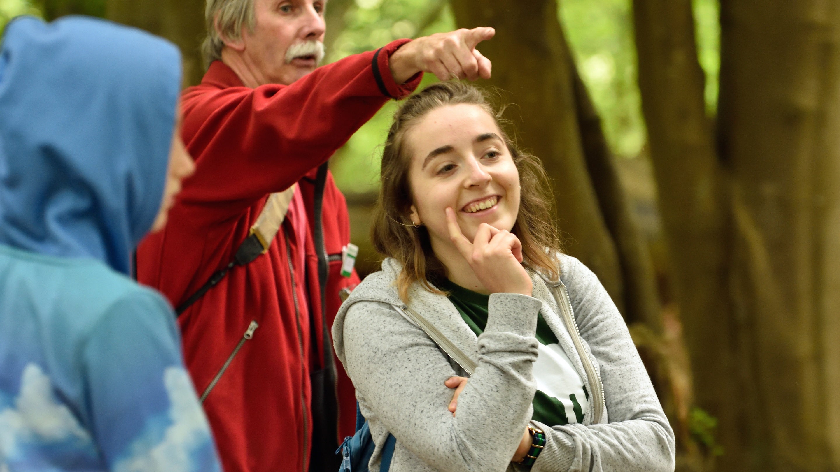 A female visitor smiling and looking to the right, with a volunteer behind pointing something out to her