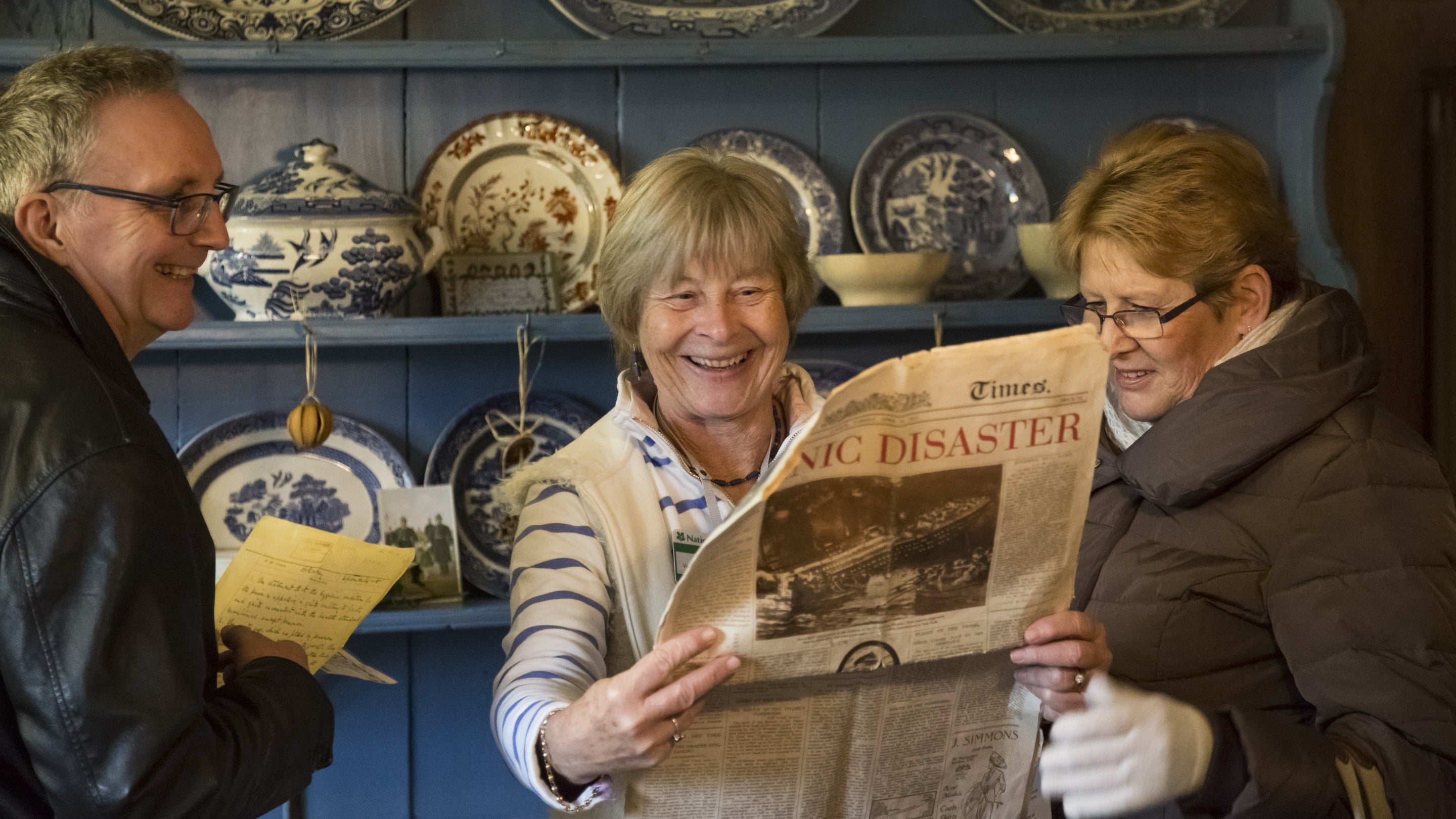 Visitors and room guide reading an archive newspaper in the Kitchen at Avebury Manor, Wiltshire