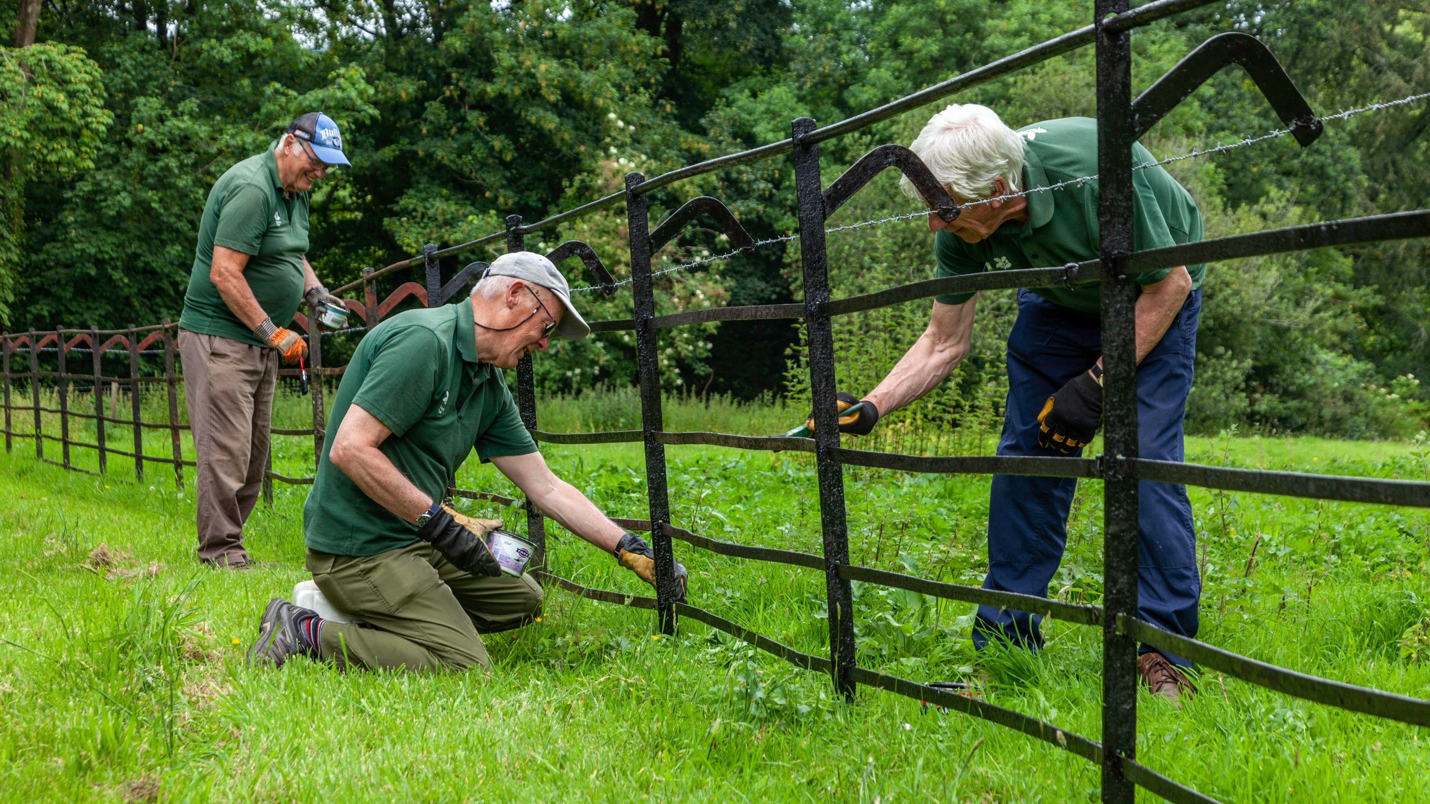 Three volunteers are intently painting a black metal fence