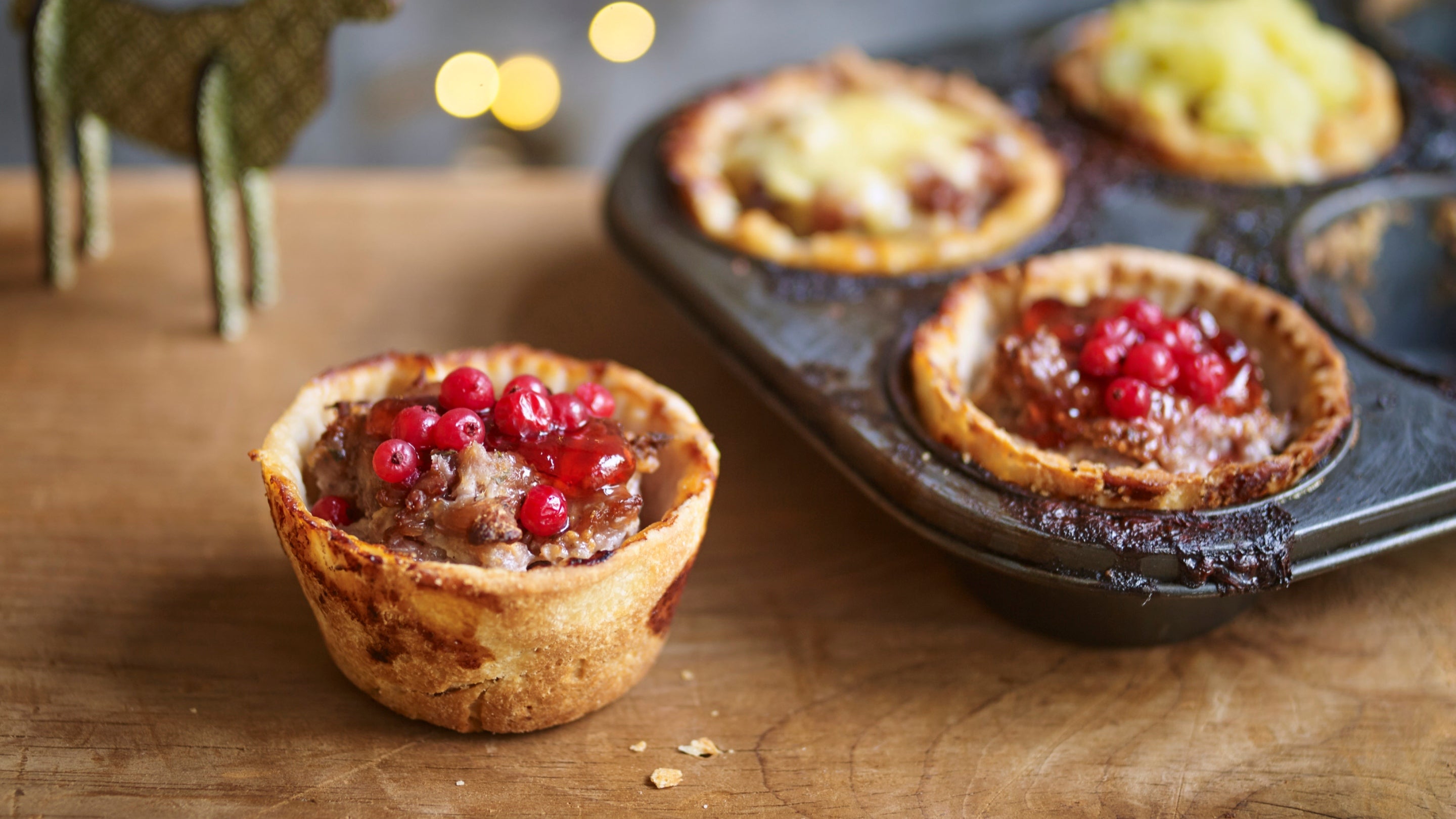 Artisan pork pie on wooden table top with more pies in a baking tray to one side