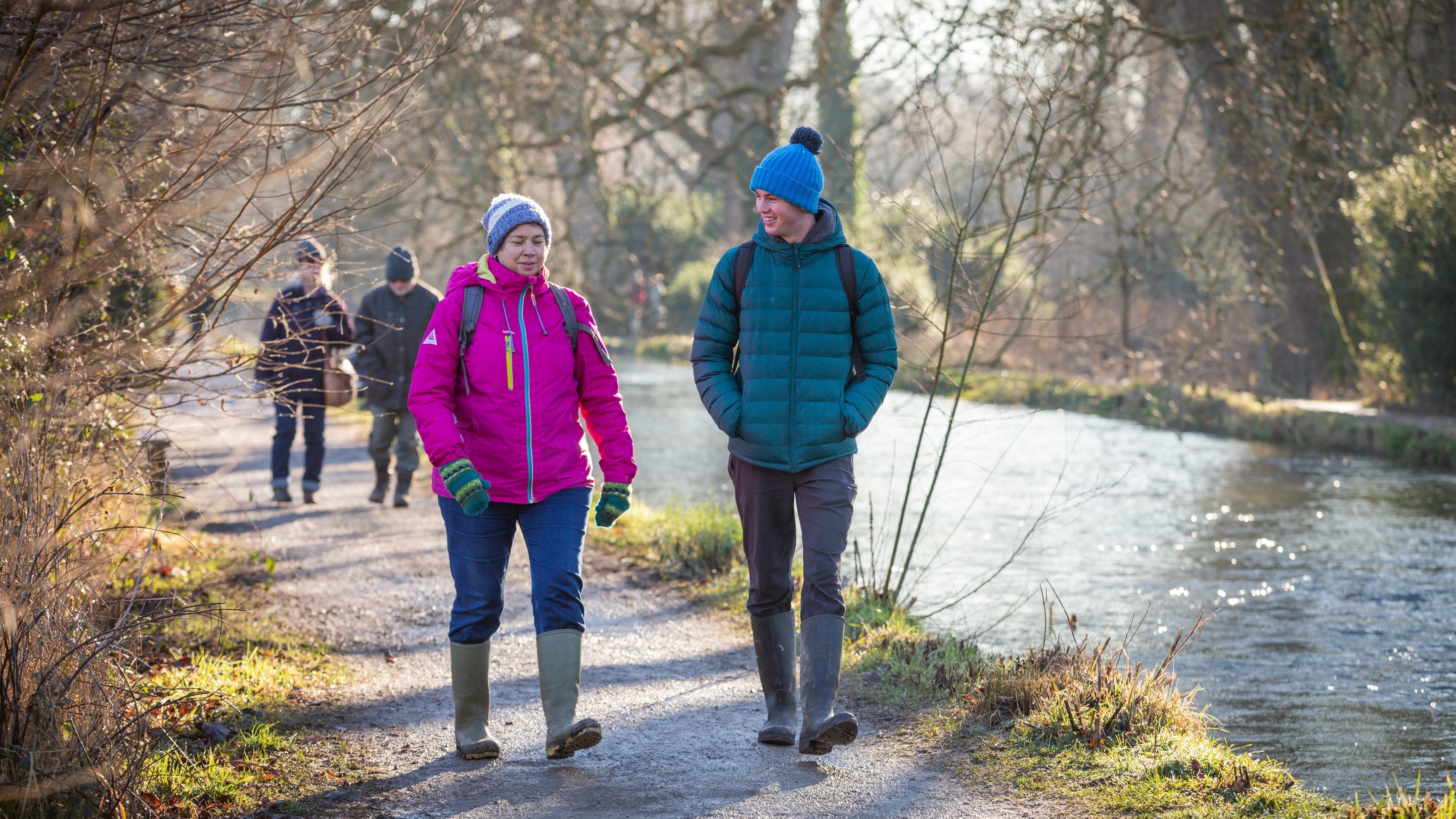 People walking beside a river with bare winter trees surrounding them.