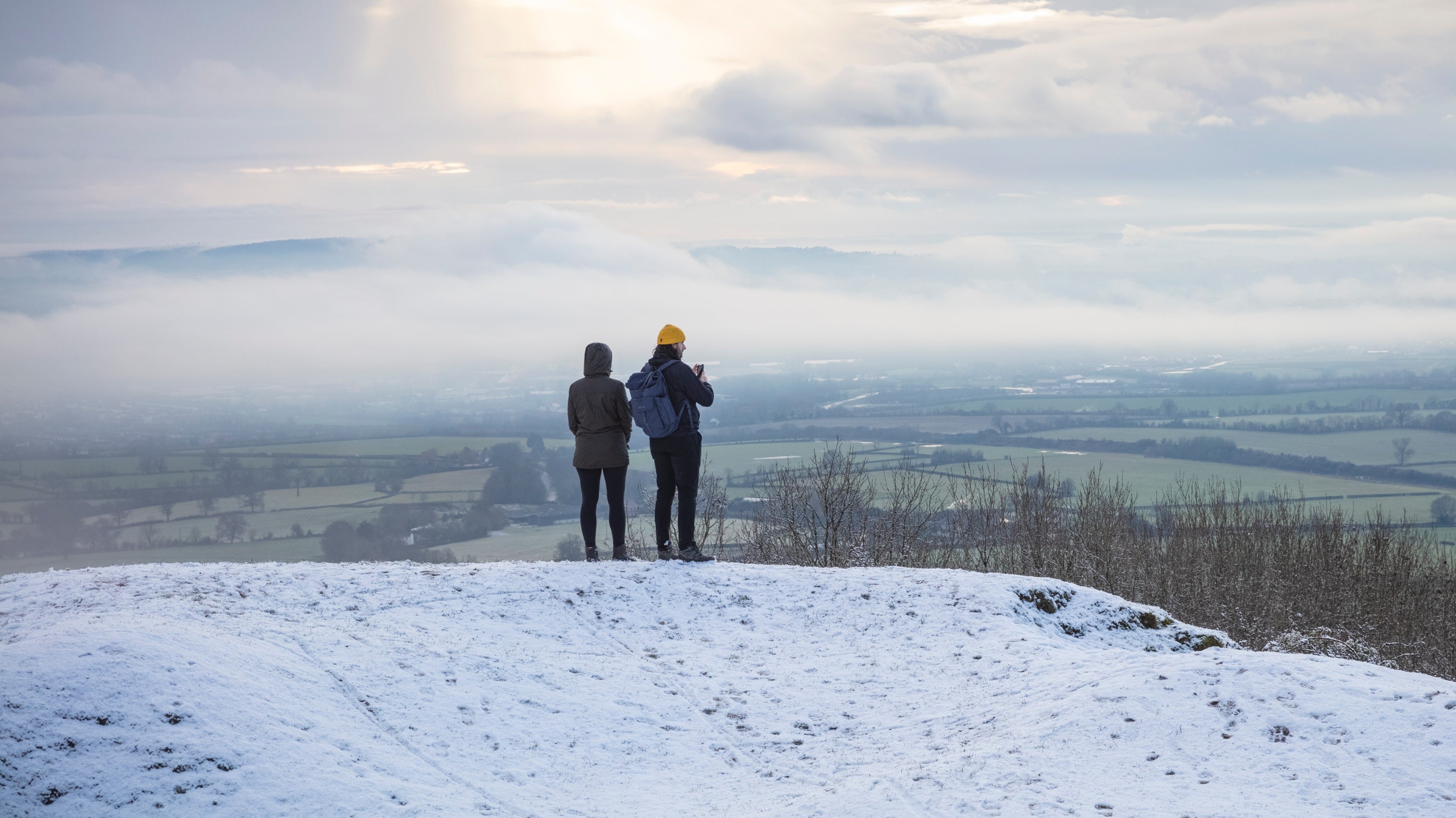 Visitors standing on a hill looking at a misty valley during a winter walk