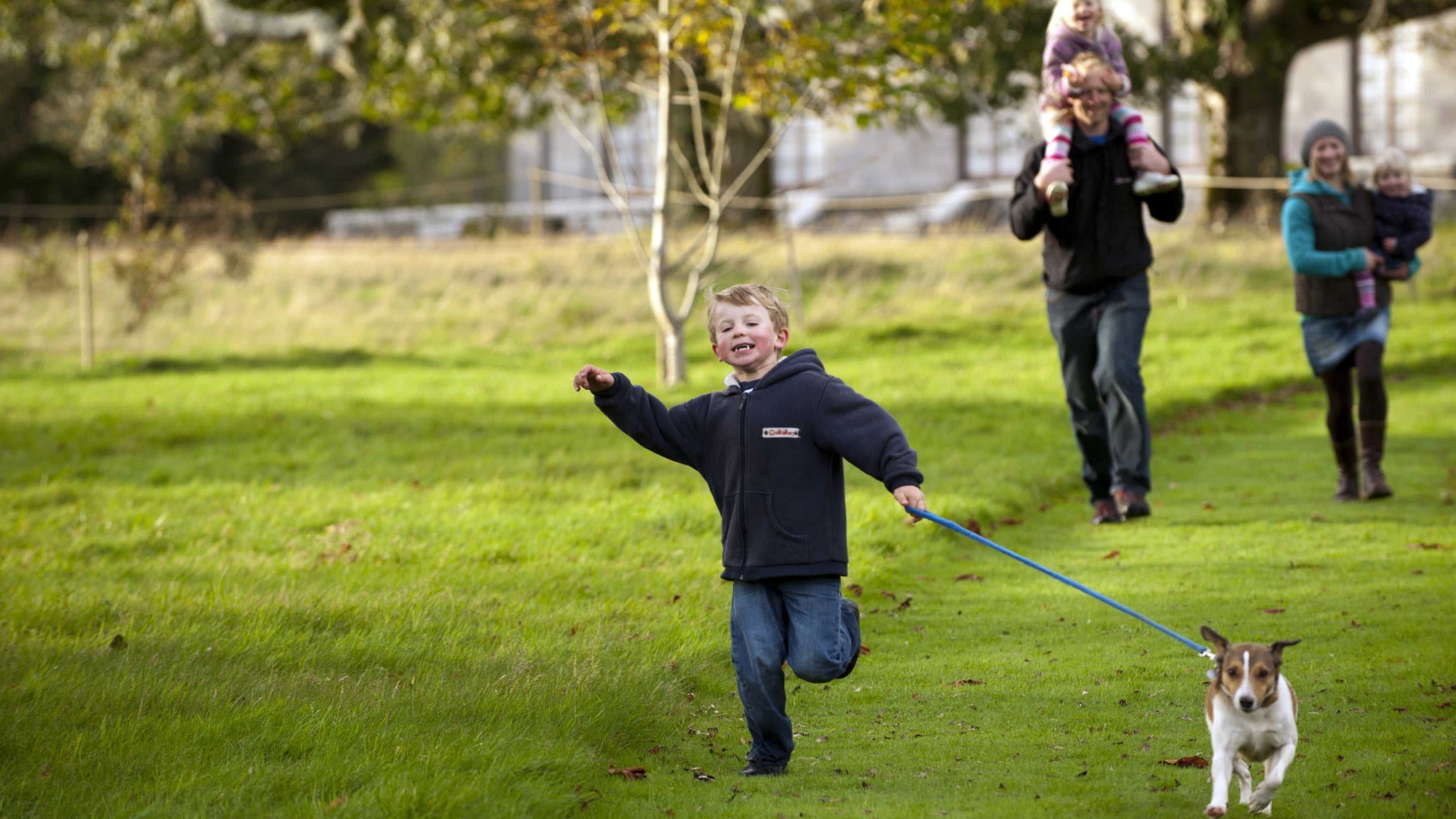 A child and little dog running, with a family walking behind, at the grounds at Arlington Court, Devon