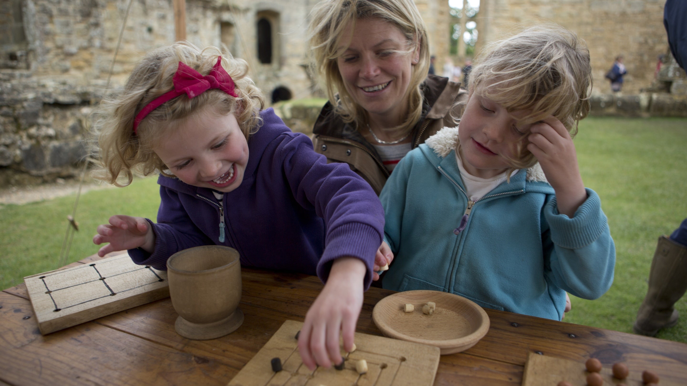 Two children playing wooden board games facing the camera with their mother sat behind and between them
