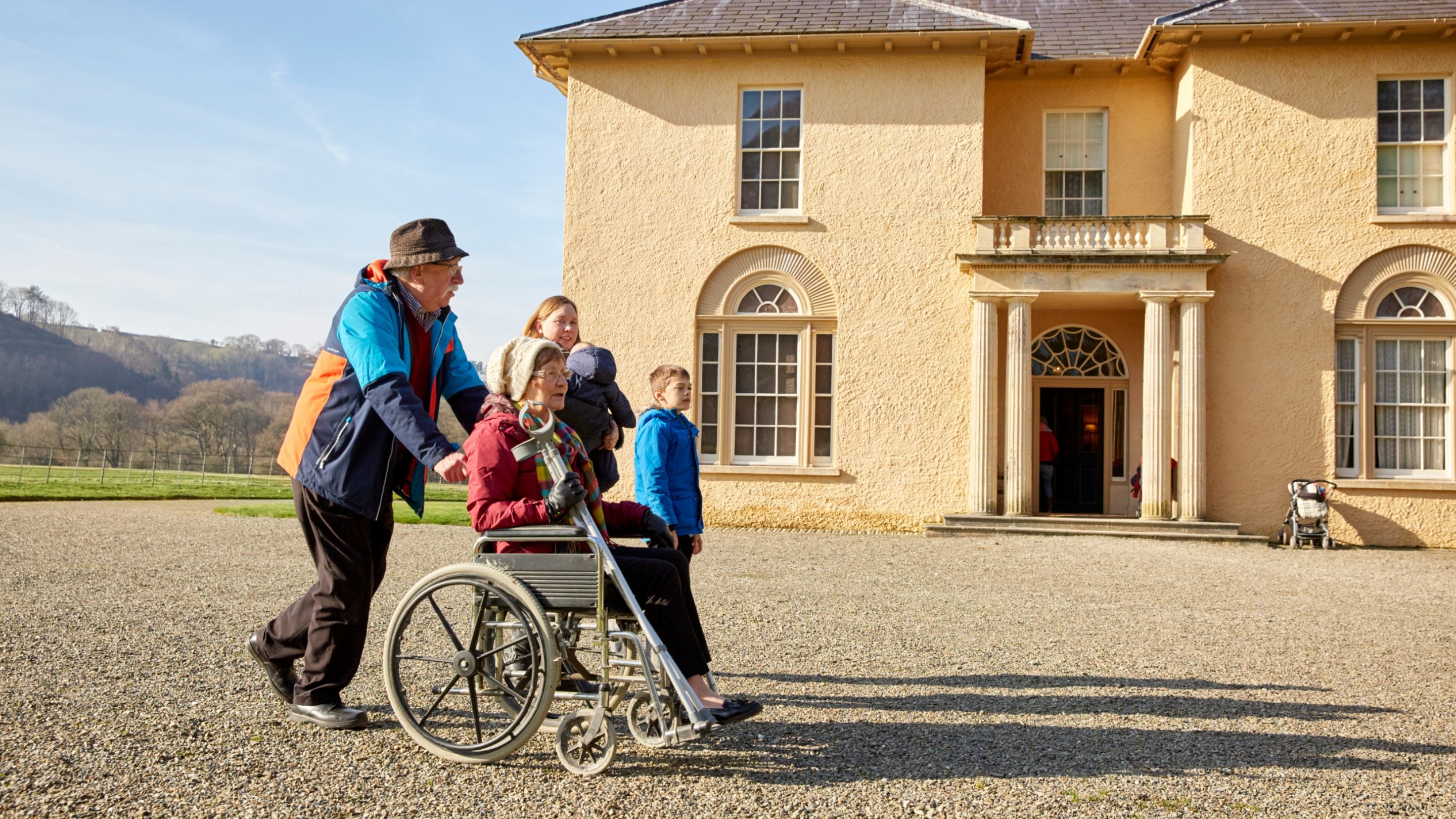 A family walking with a lady in a wheelchair in front of the villa at Llanerchaeron, Wales