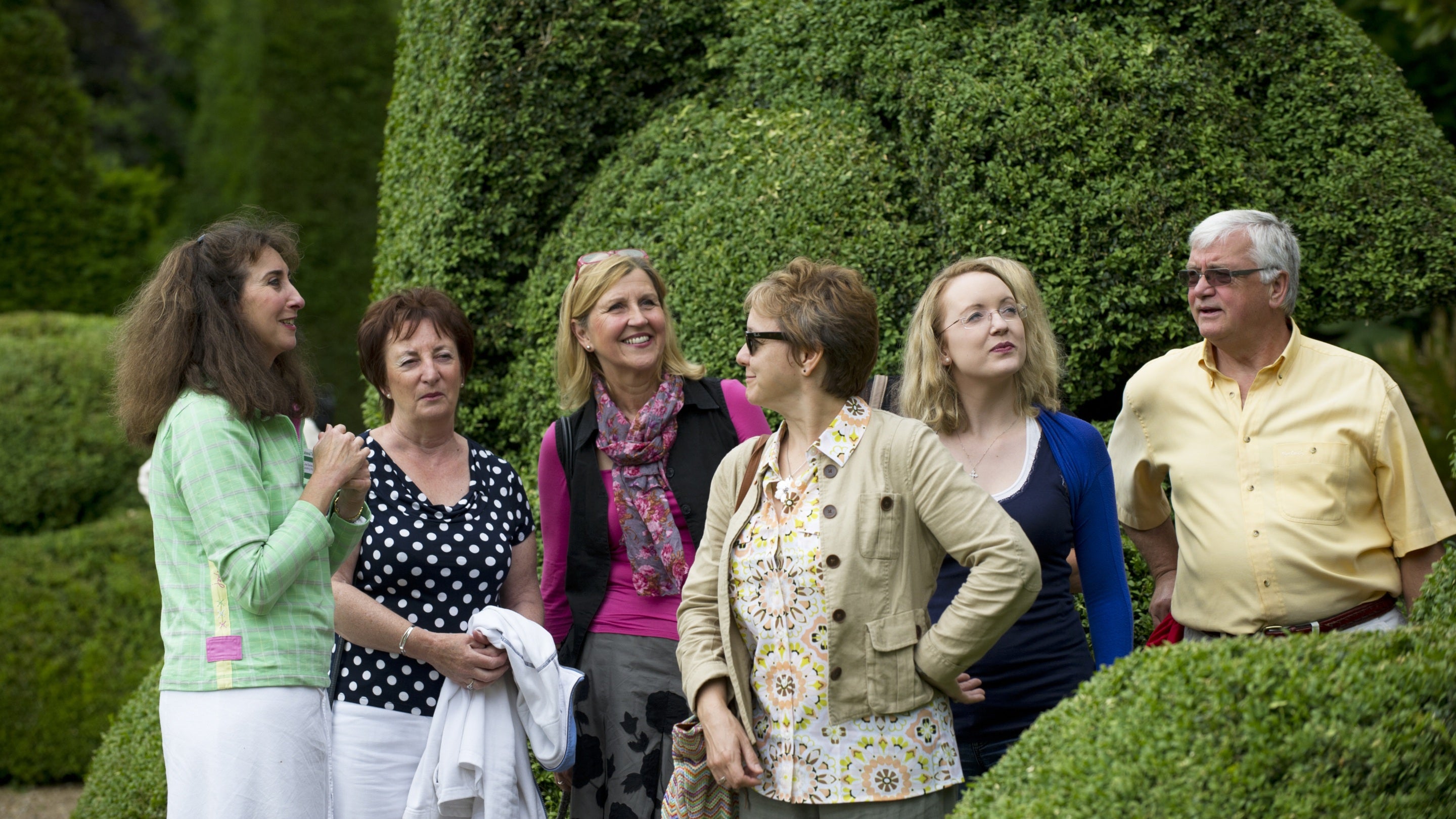 Close-up of a group of people surrounded by topiarised hedging in the sun listening to a guide