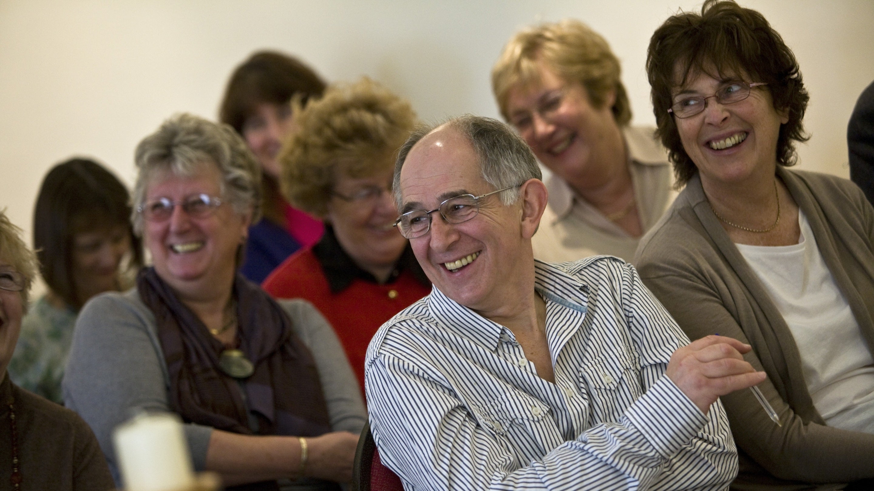A group of people sat laughing and smiling in a lecture at Petworth House in Sussex.