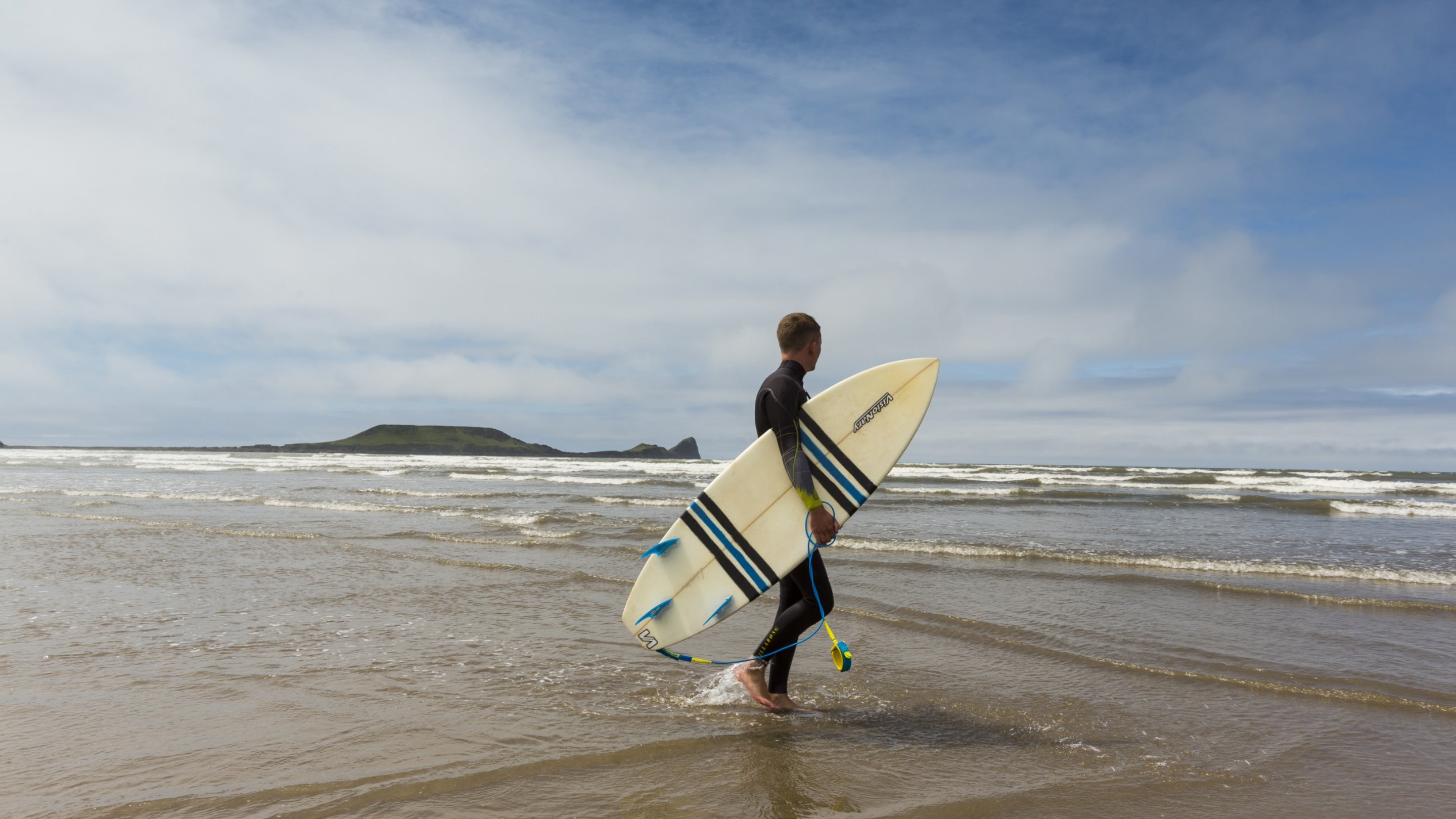 Surfer holding their board on Rhosili beach, Gower Peninsula, Wales