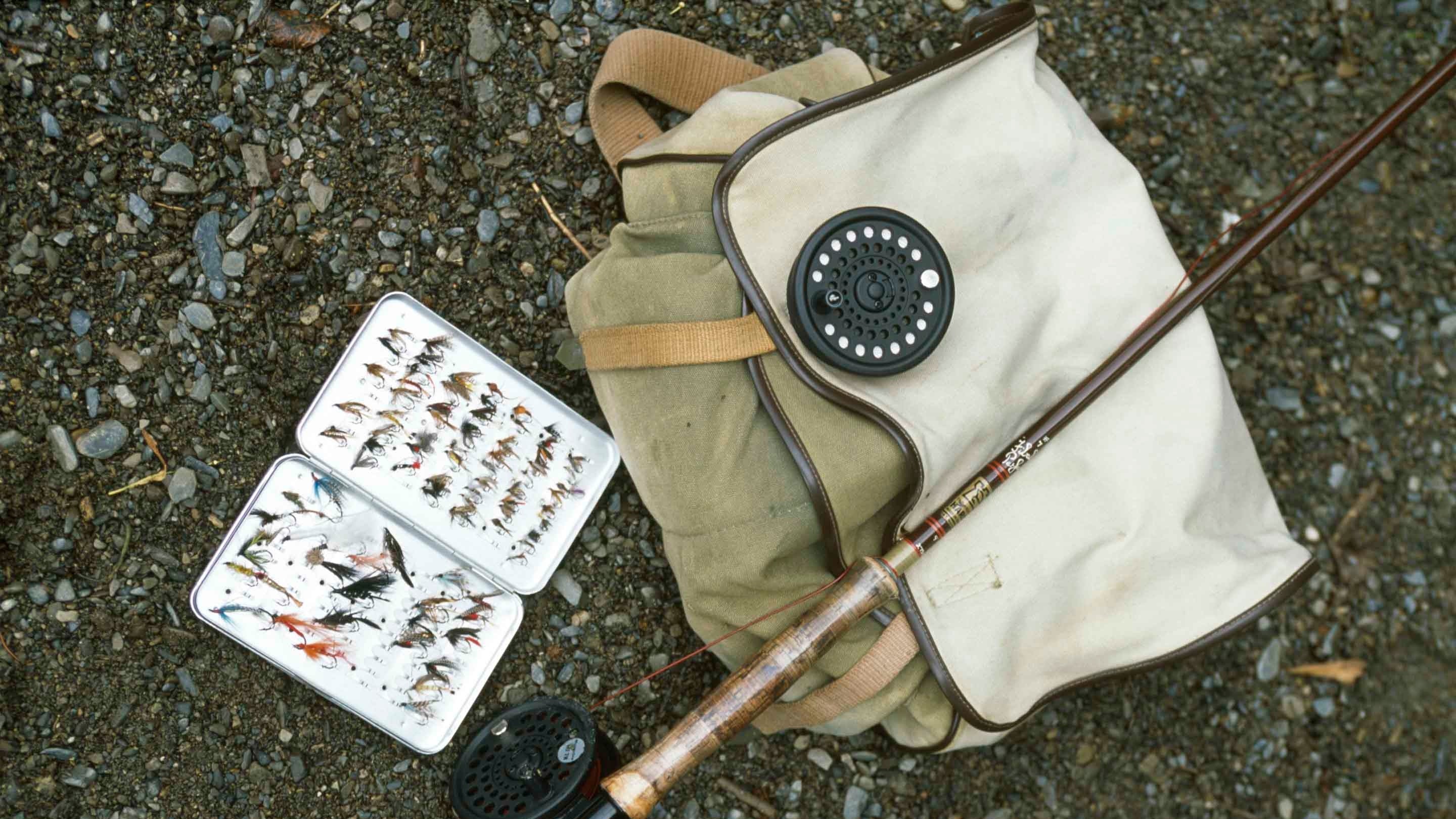 A selection of fishing equipment comprising a rod, reels, a box of flies and haversack laid out on the shingle beach at Loweswater in the Buttermere Valley, Lake District