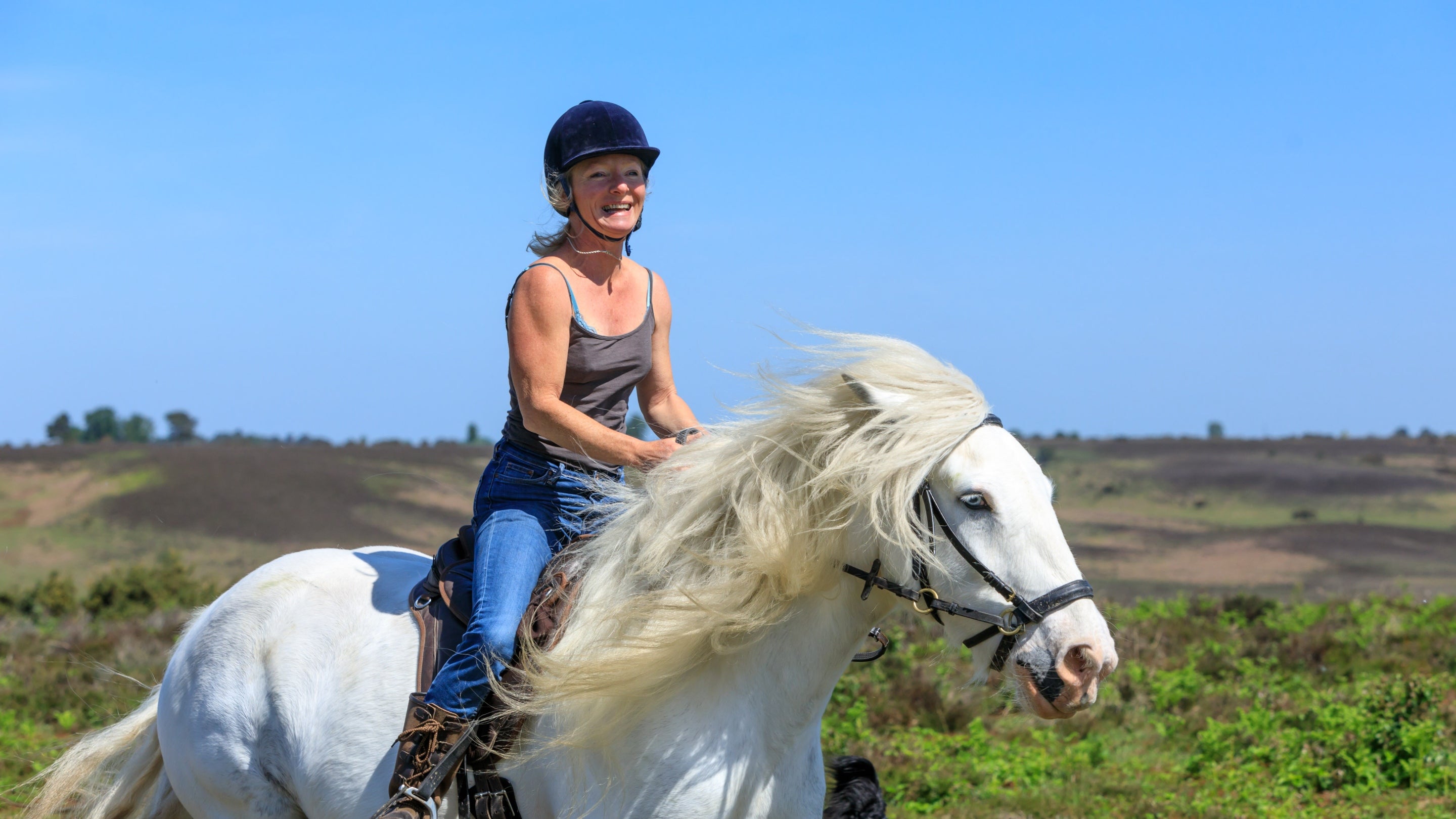 A smiling visitor rides a grey horse on Rockford Common in the New Forest, Hampshire