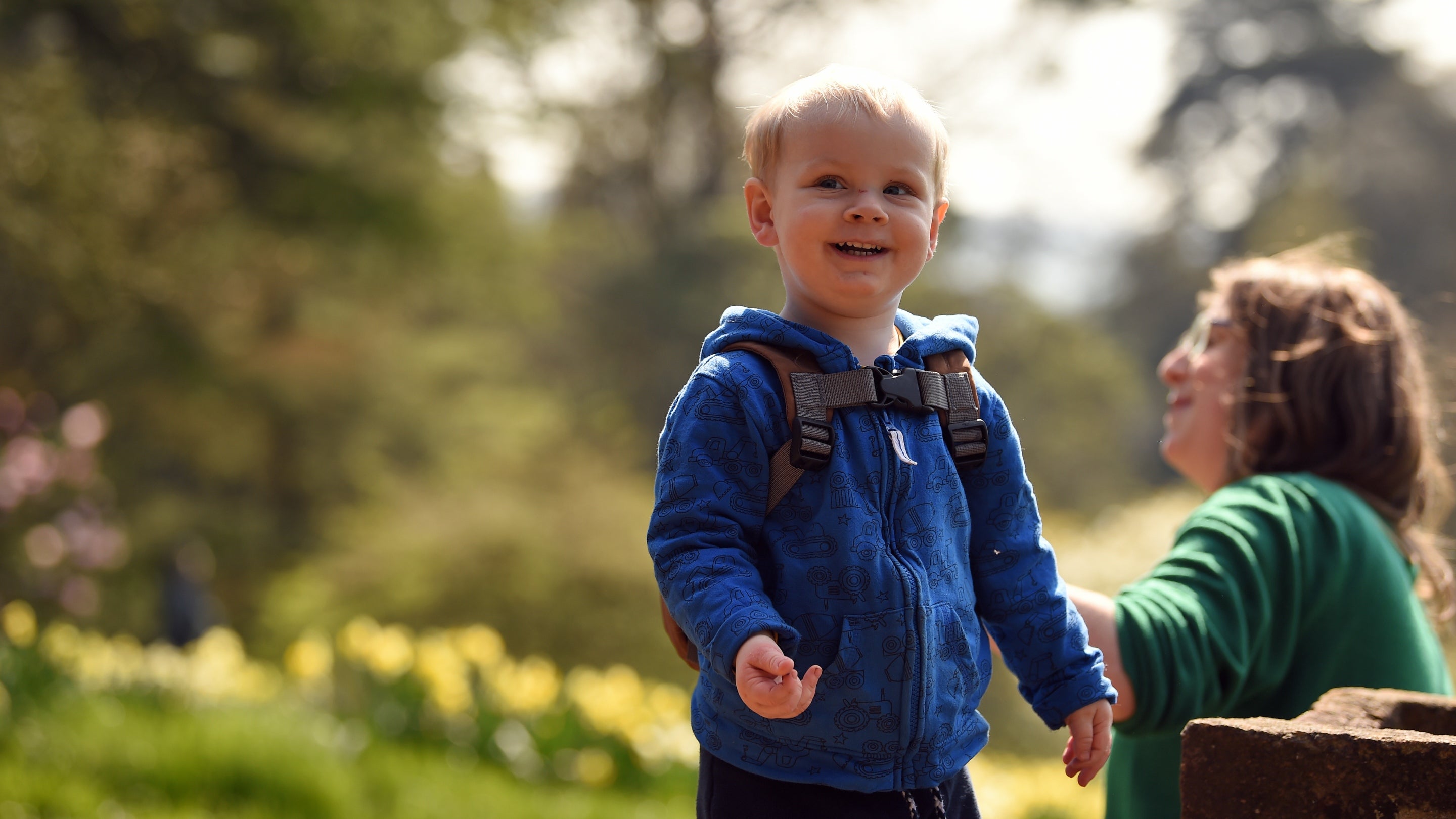 Mother and son look at a terracotta flowerpot planted with colourful spring flowers, in the garden in spring at Knightshayes, Devon
