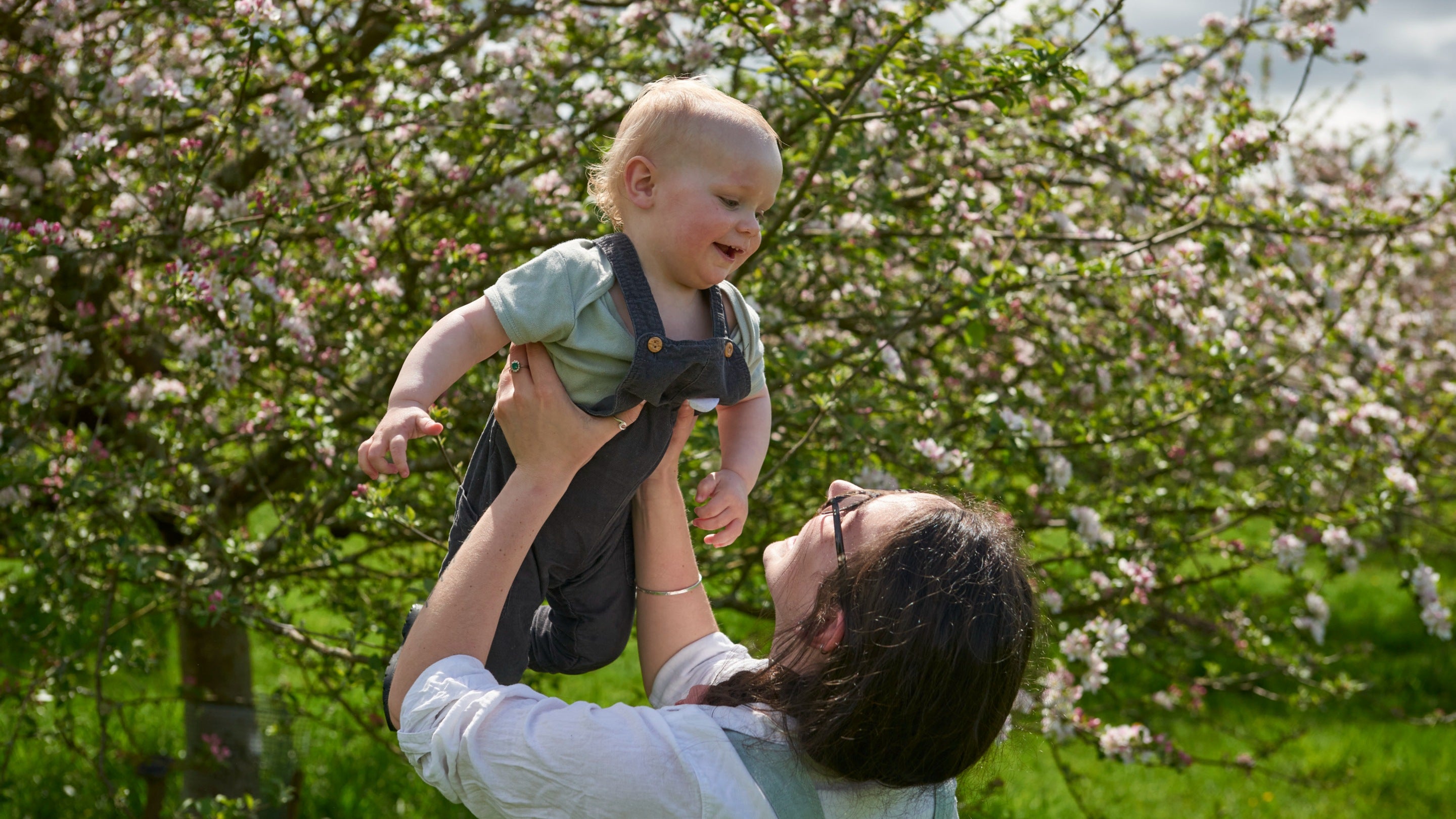 A woman holding up her child with a blossom tree behind them in the Orchard at Cotehele, Cornwall