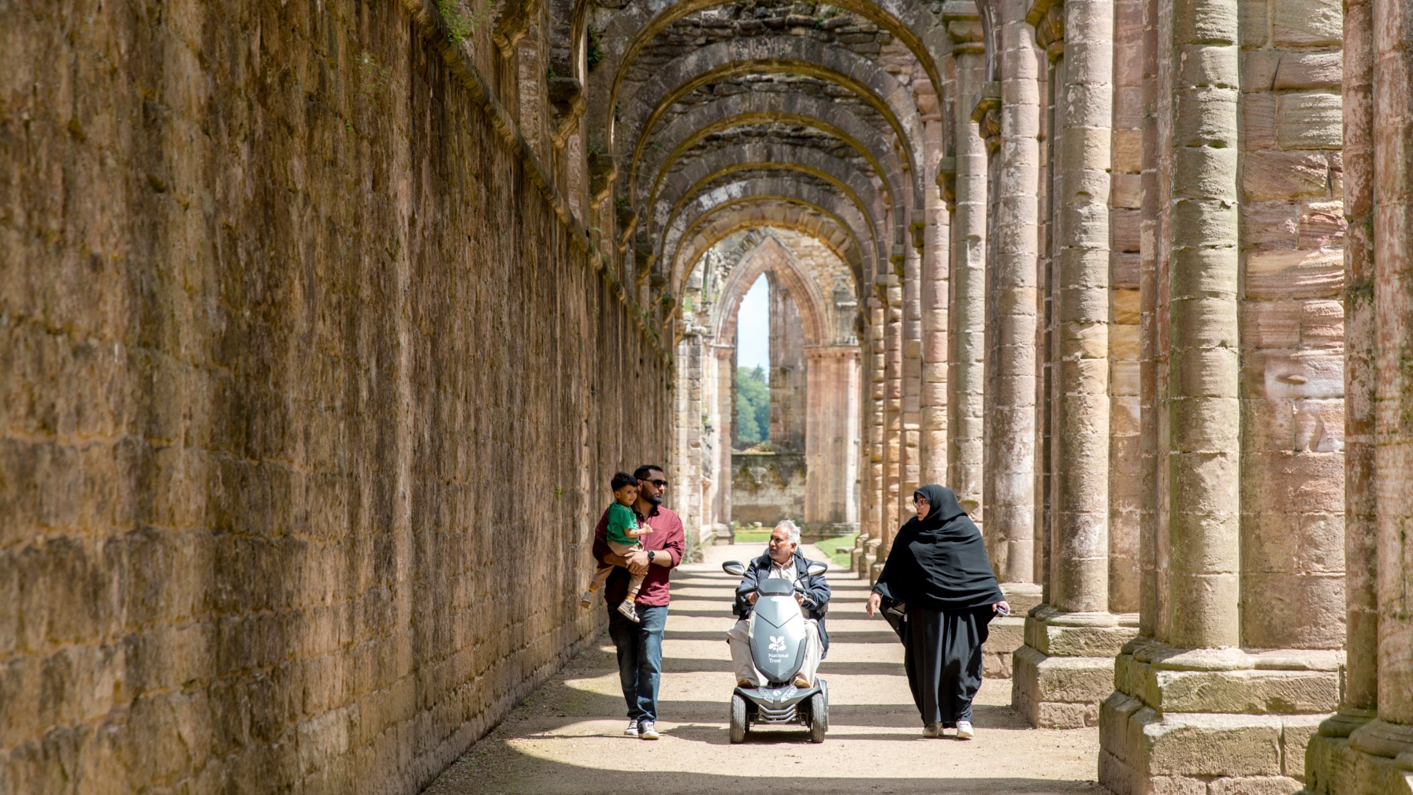 Three visitors exploring inside Fountains Abbey and Studley Royal Water Garden, North Yorkshire
