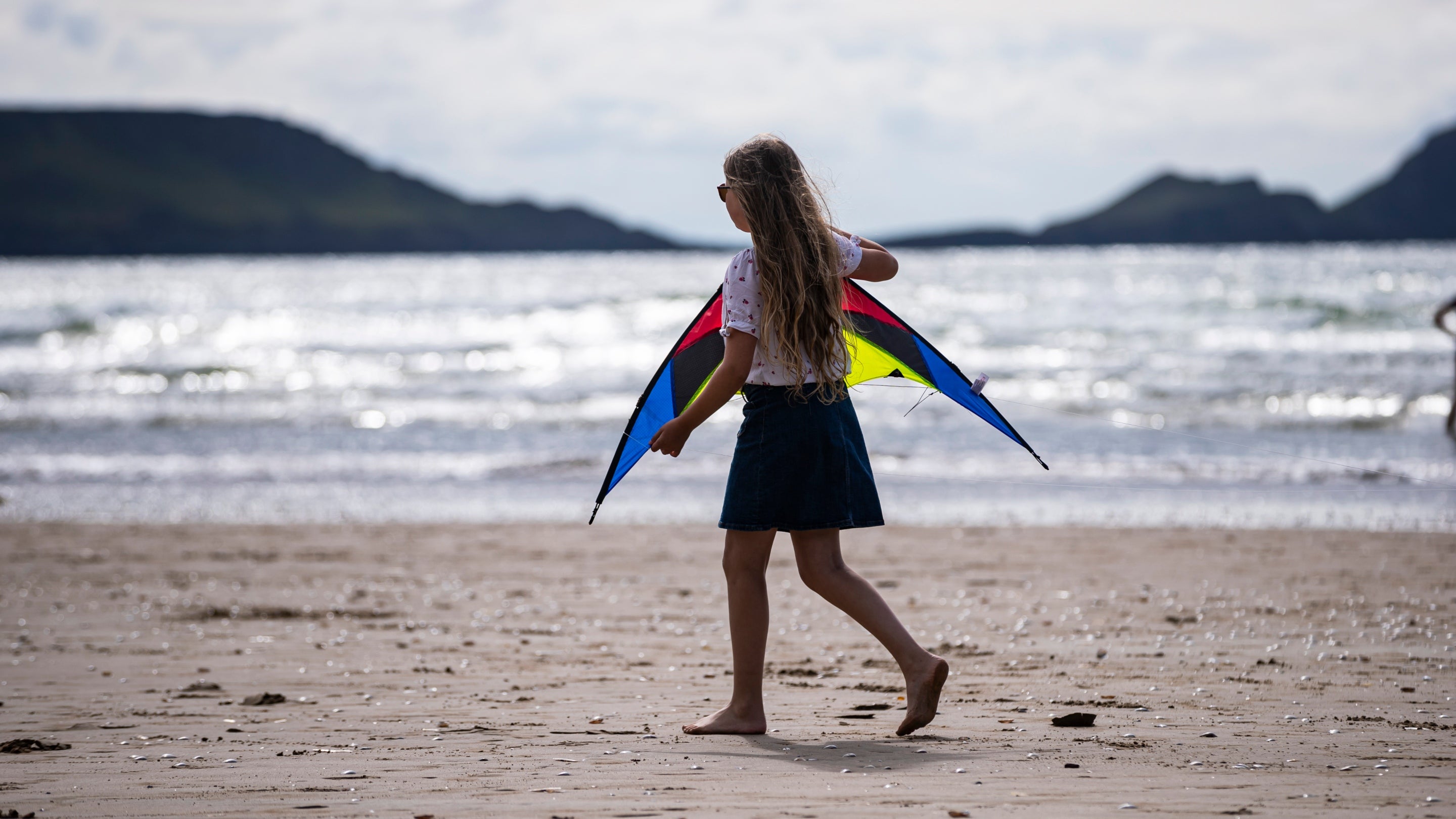A child walks along the beach with a kite at Rhosili and South Gower Coast Wales