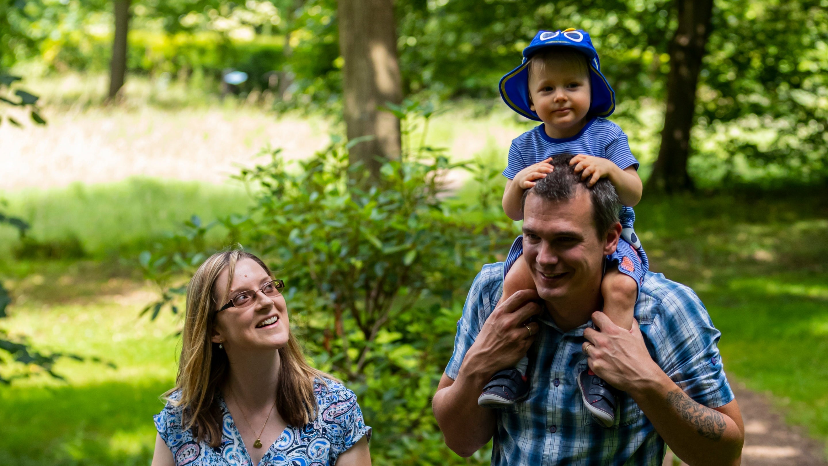 Two adults, one with a baby on his shoulders, walk through the grounds at Clandon Park, Surrey