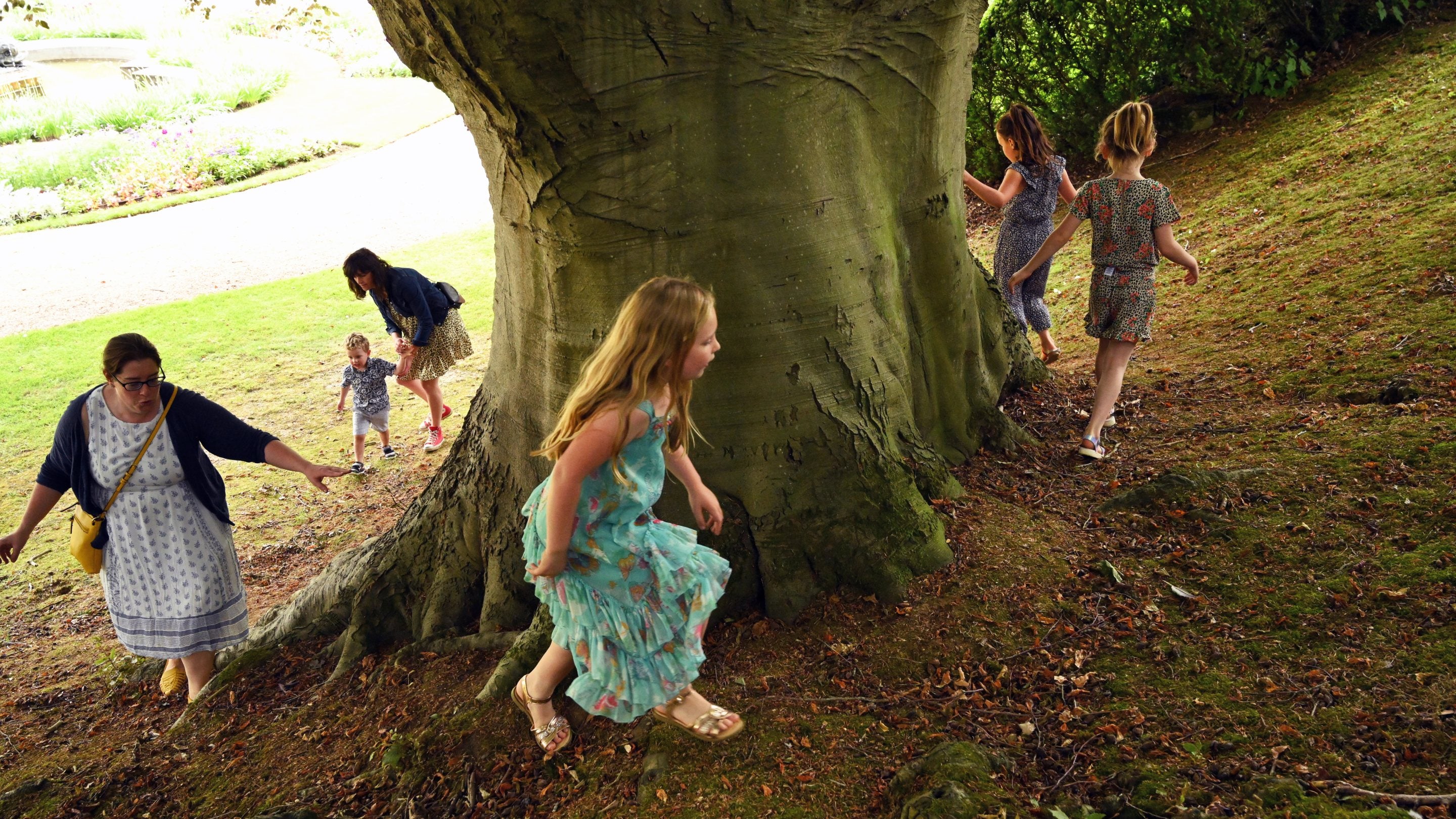 Adults and children play around a large tree in the garden at Ascott, Buckinghamshire