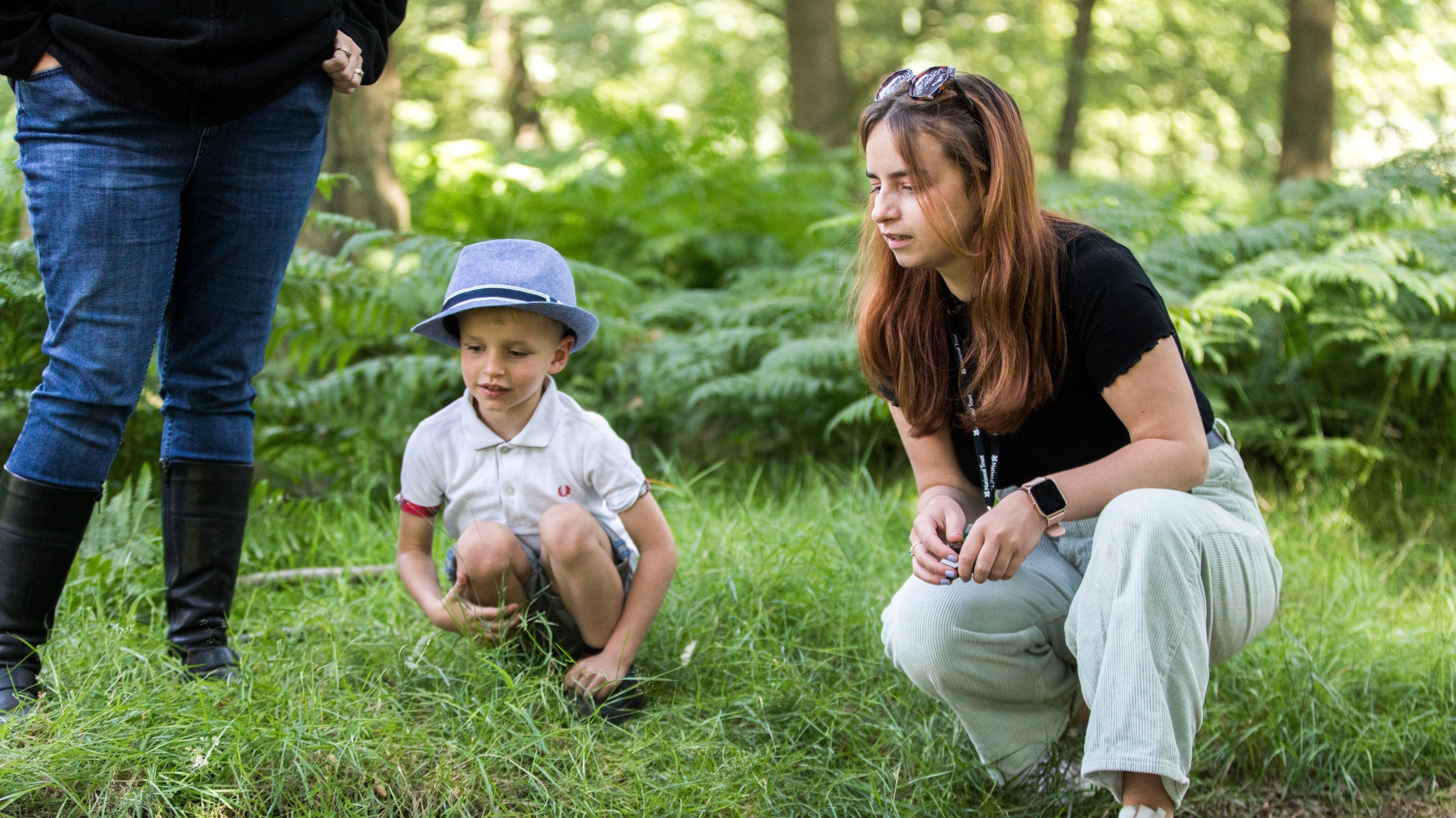 Two adults and a child explore woodland as part of the summer activity programme at Dunham Massey, Cheshire