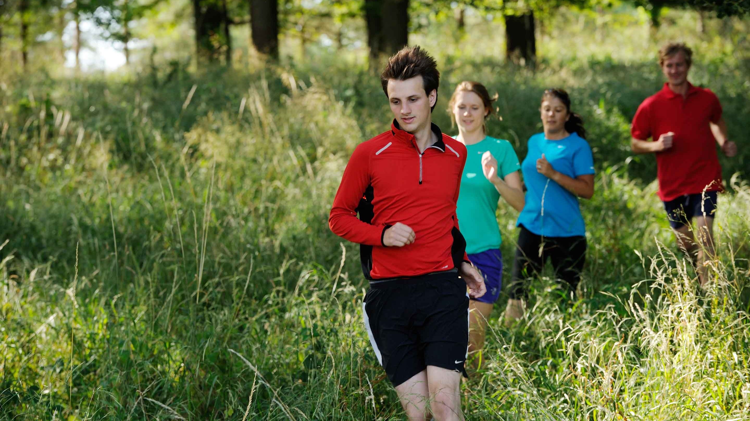 A group of runners running through the long grass in a wooded area