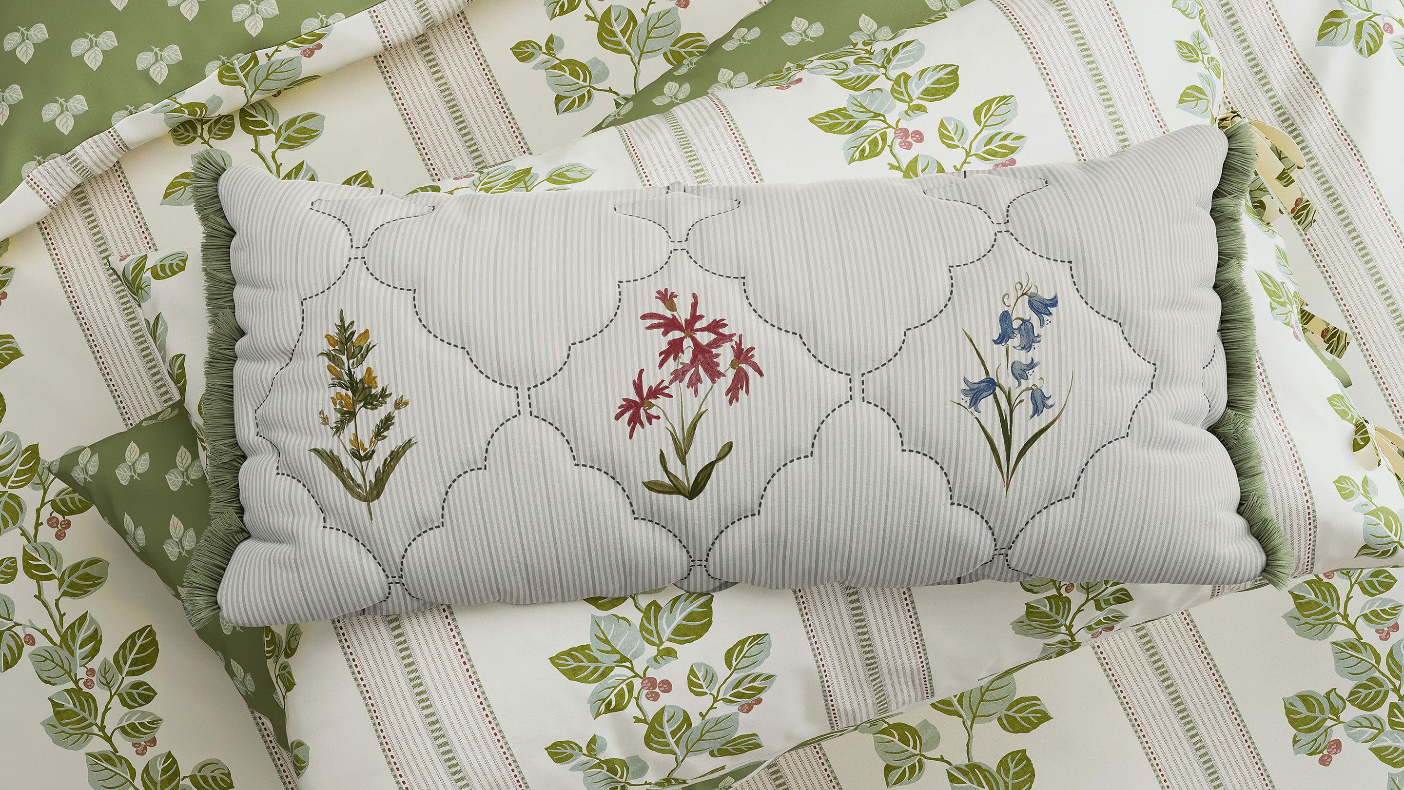 A pillow with a scallop pattern and flowers sits on patterned bed lining