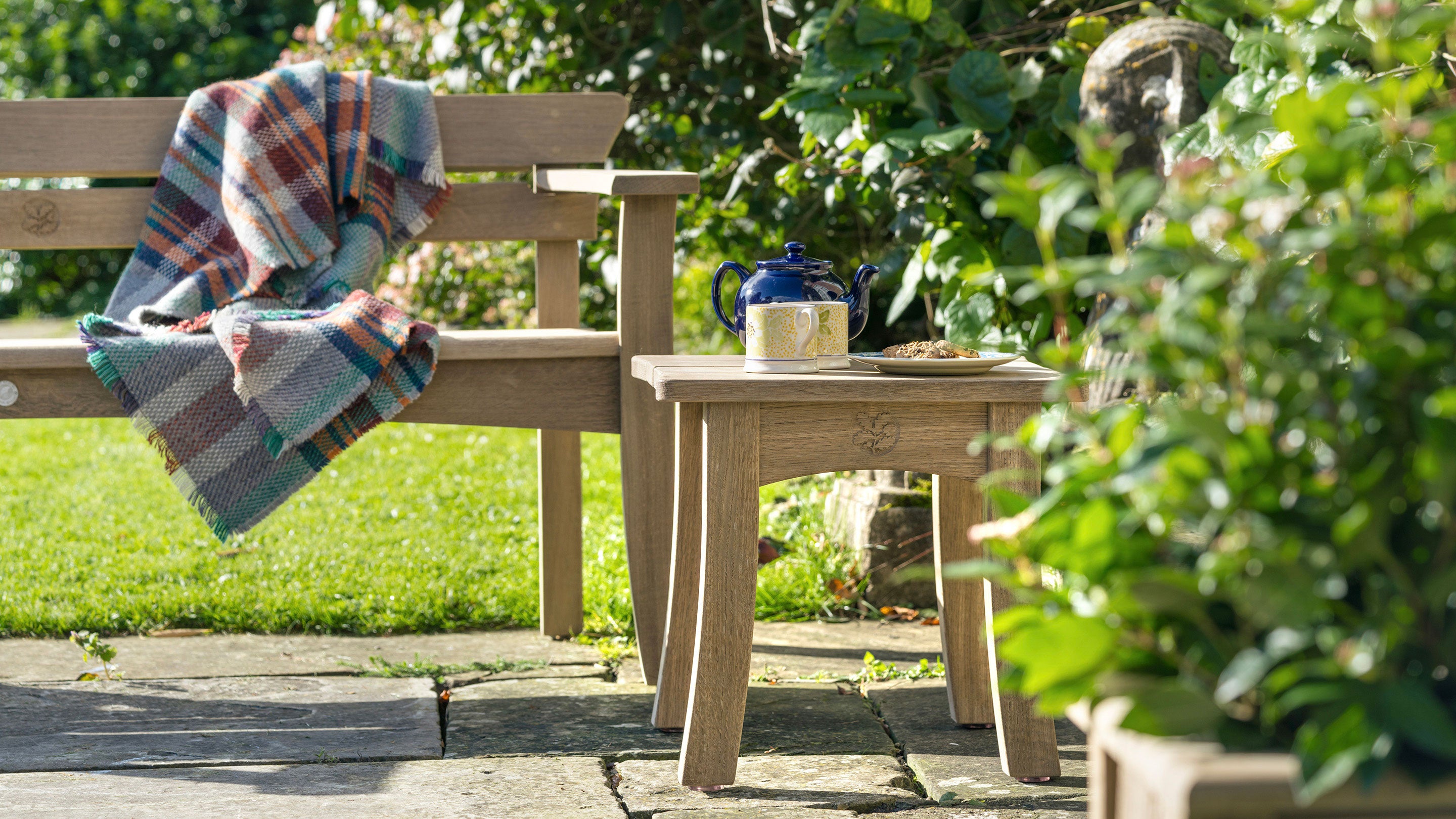 Low shot of a wooden bench and table on a stone patio surrounded by shrubbery