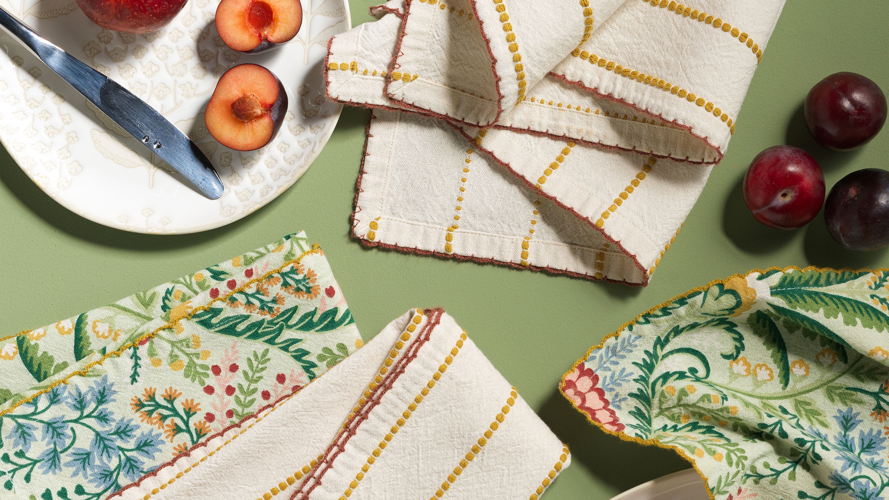 Patterned kitchen textiles and a patterned plate on a green table with fruit