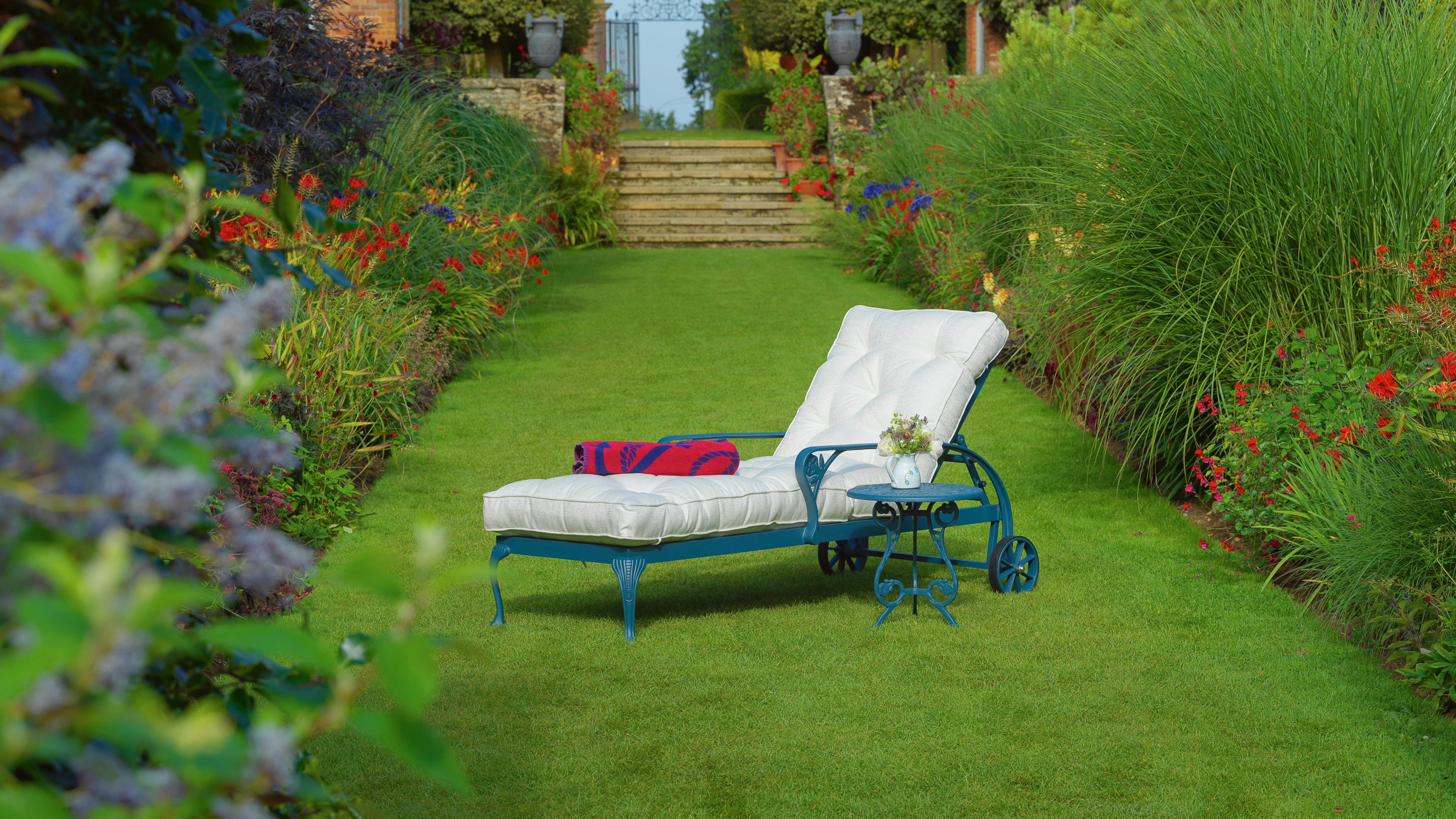 Garden lounger on grass surrounded by plants blooming in spring