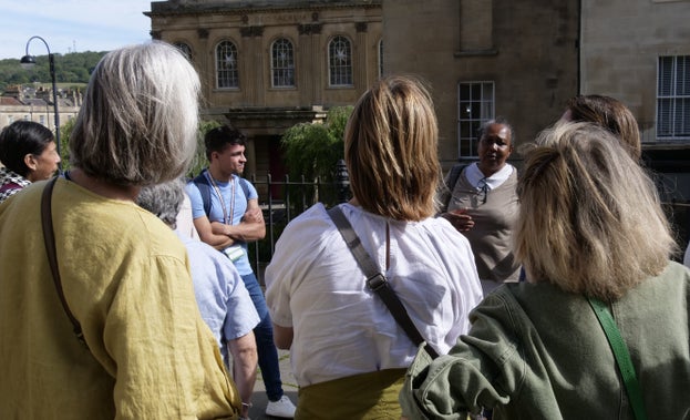 A group of people are stood on a street in Bath collected around Tim and Pauline who are talking about the history of Bath