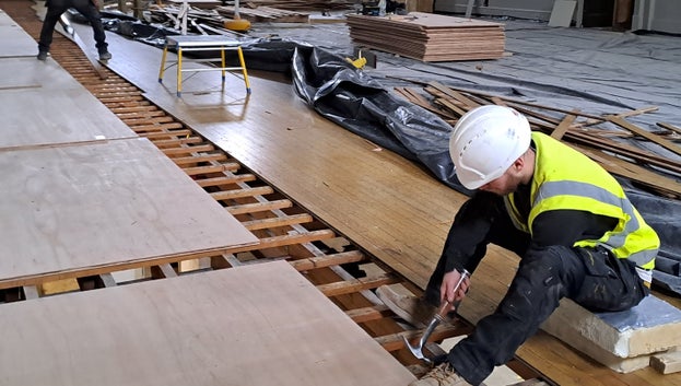 People can be seen holding hammers, straddling the floorboards as they lift each one up.