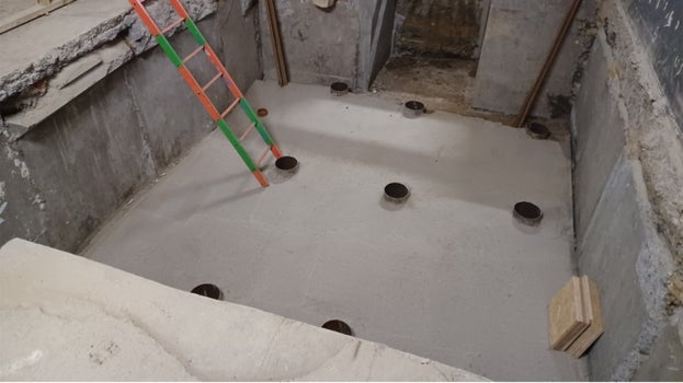 A view into the floor of the lift pit showing smooth grey concrete with a few metal poles on show and a ladder.