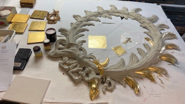 One mirror is on a table with samples of gilding materials, these are being tested on the mirror to decide which option to go with.