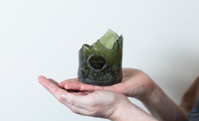 In the palm of a hand sits the bottom third of a broken Georgian wine bottle. The glass is dark green and is embossed with the name DOLTON